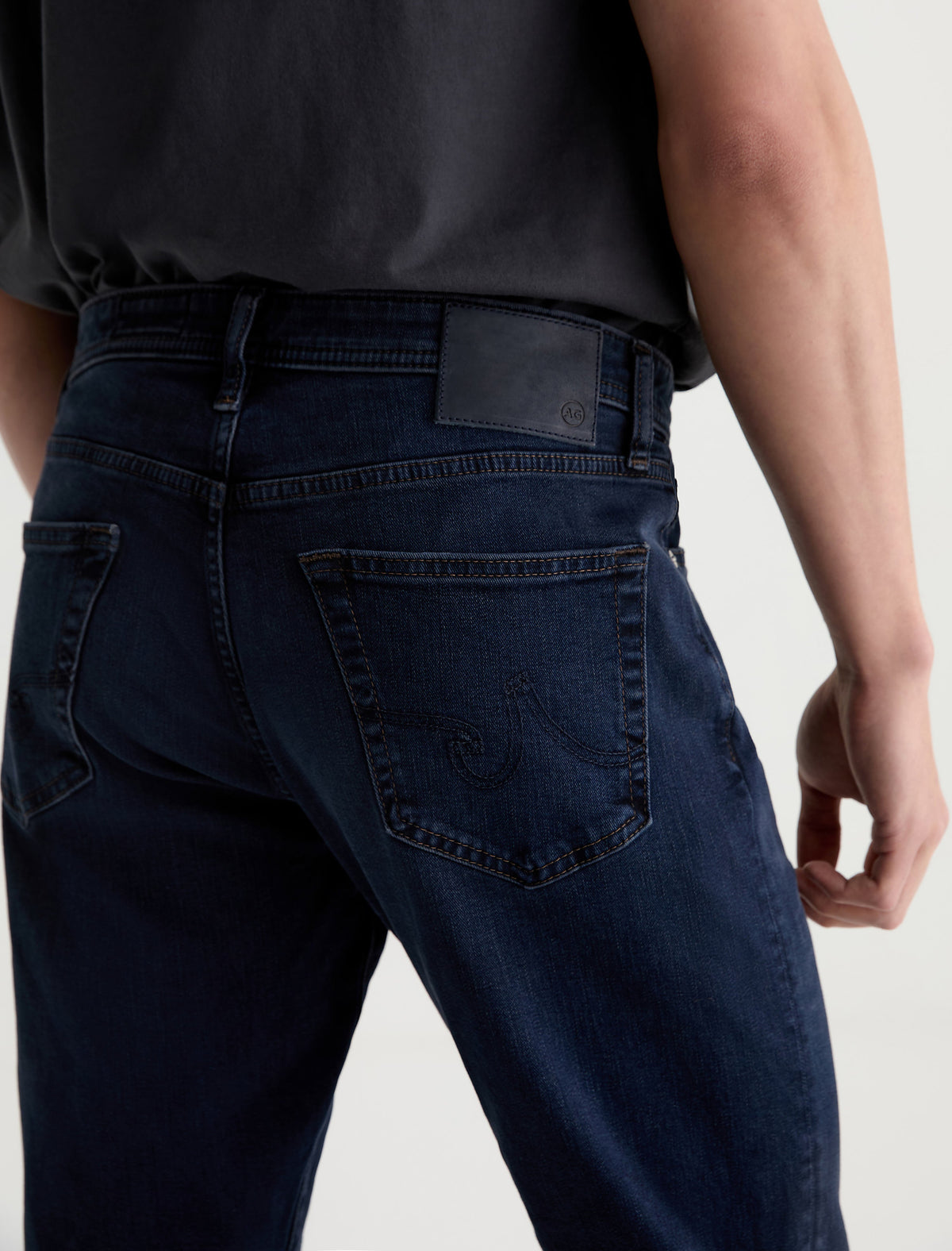 Close-up back view of AG Graduate dark indigo blue denim jeans with embroidered pocket