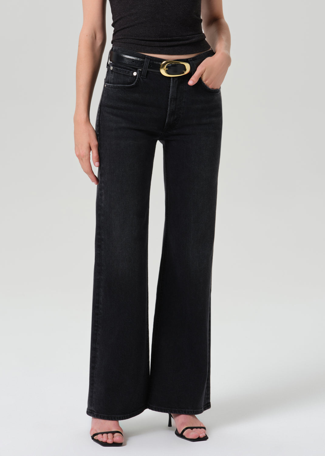 Model wearing Citizens of Humanity Kimberly 70s Flare jeans in dark washed black with wide leg silhouette and gold belt bu...
