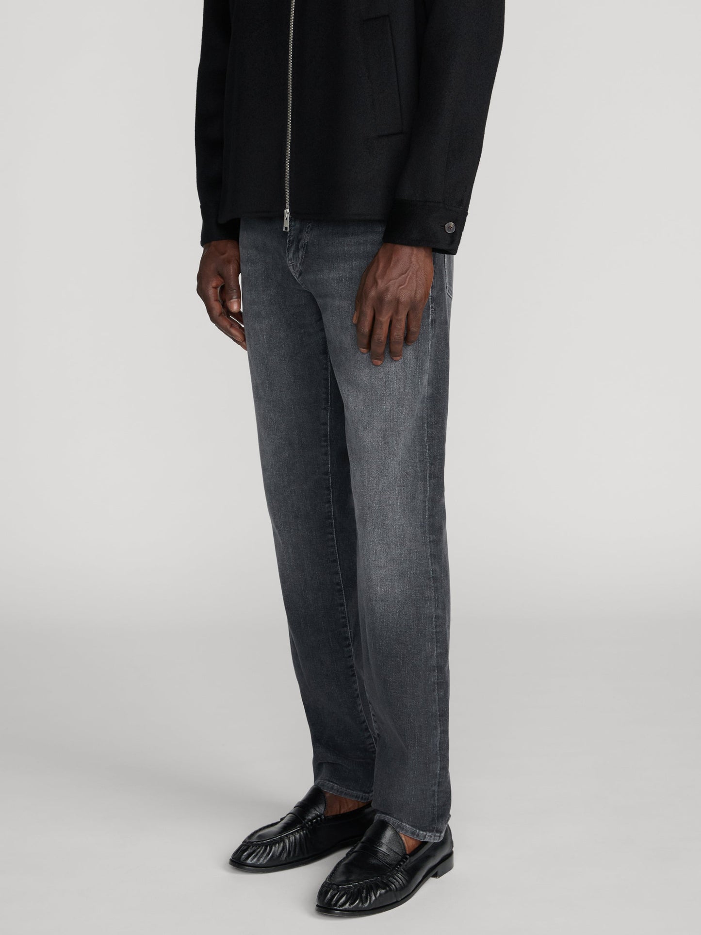Model wearing Frame L'Homme Slim jeans in dark washed grey with black jacket and loafers