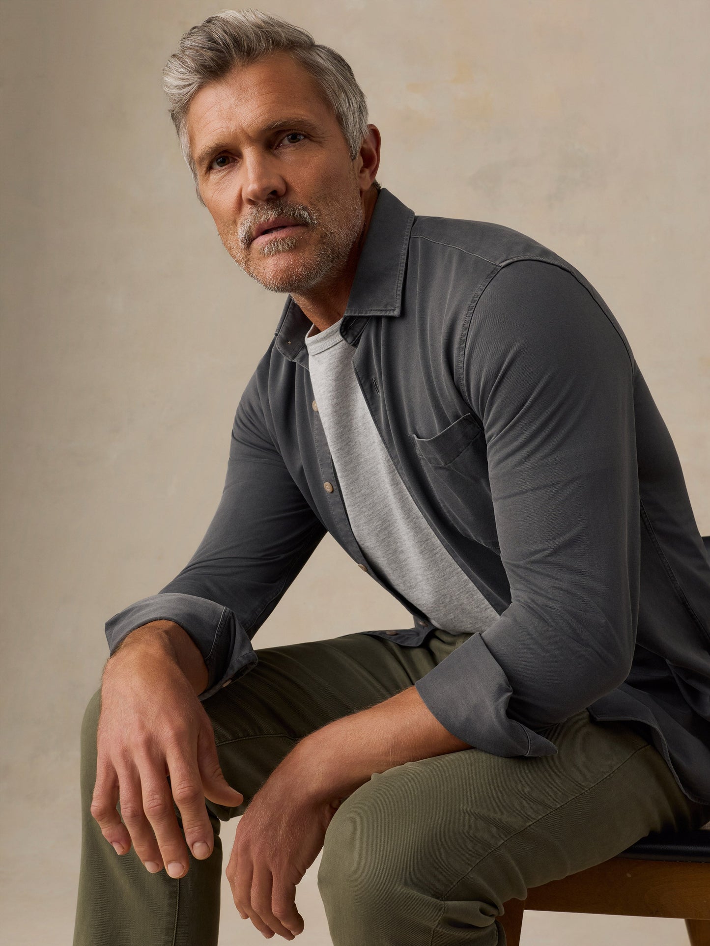 Male model seated wearing Faherty Costa Piqué Shirt in dark charcoal Ridge Black over gray tee