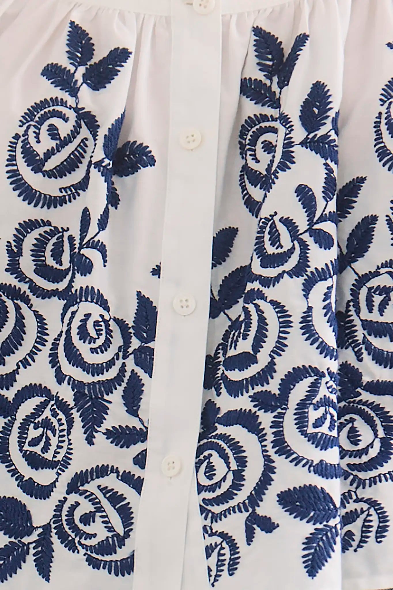 Close-up of white button-up top featuring blue embroidered rose pattern