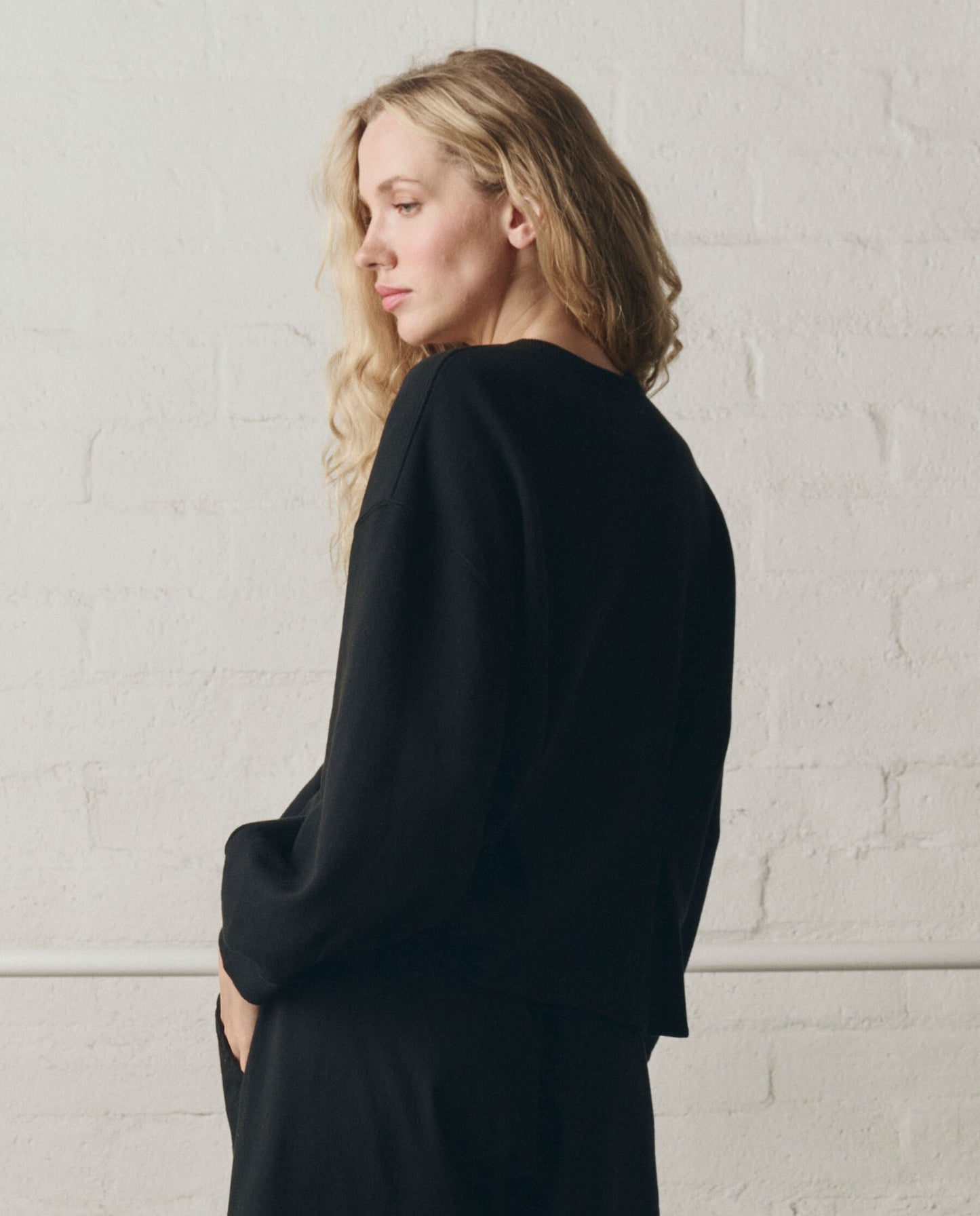 Woman wearing black slouchy corset sweatshirt in profile view against white backdrop