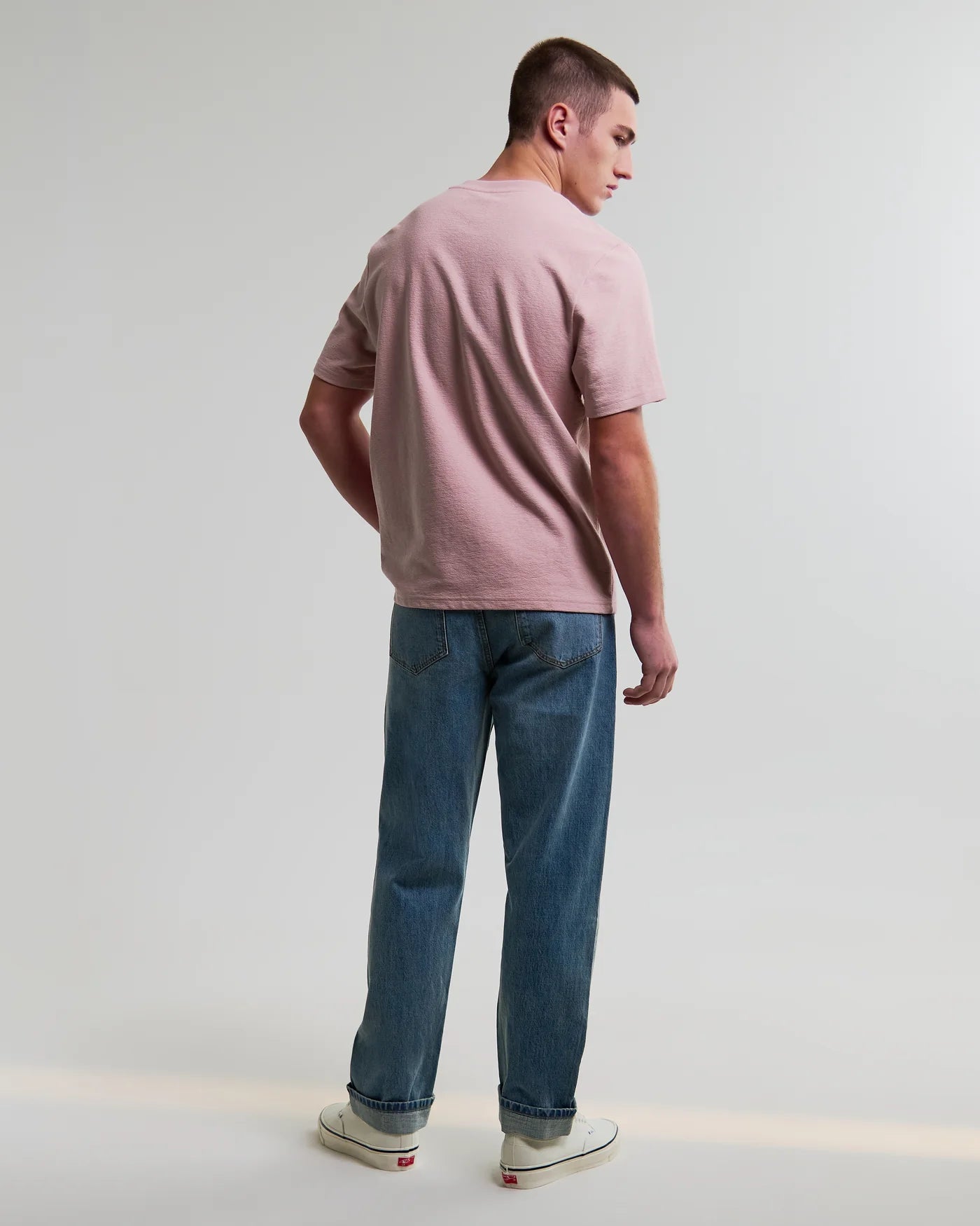 Back view of man wearing Wax London Dean short sleeve tee in dusty pink with blue jeans and sneakers.