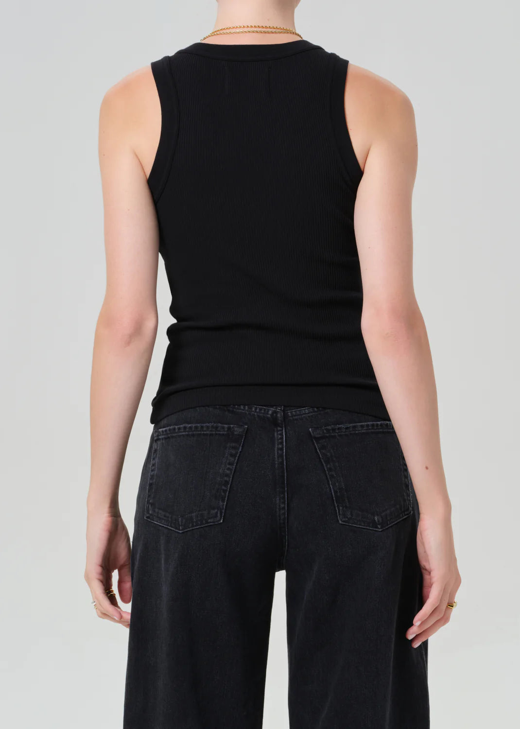 Back view of person wearing Citizens of Humanity Isabel black ribbed tank top with dark jeans and gold necklace.