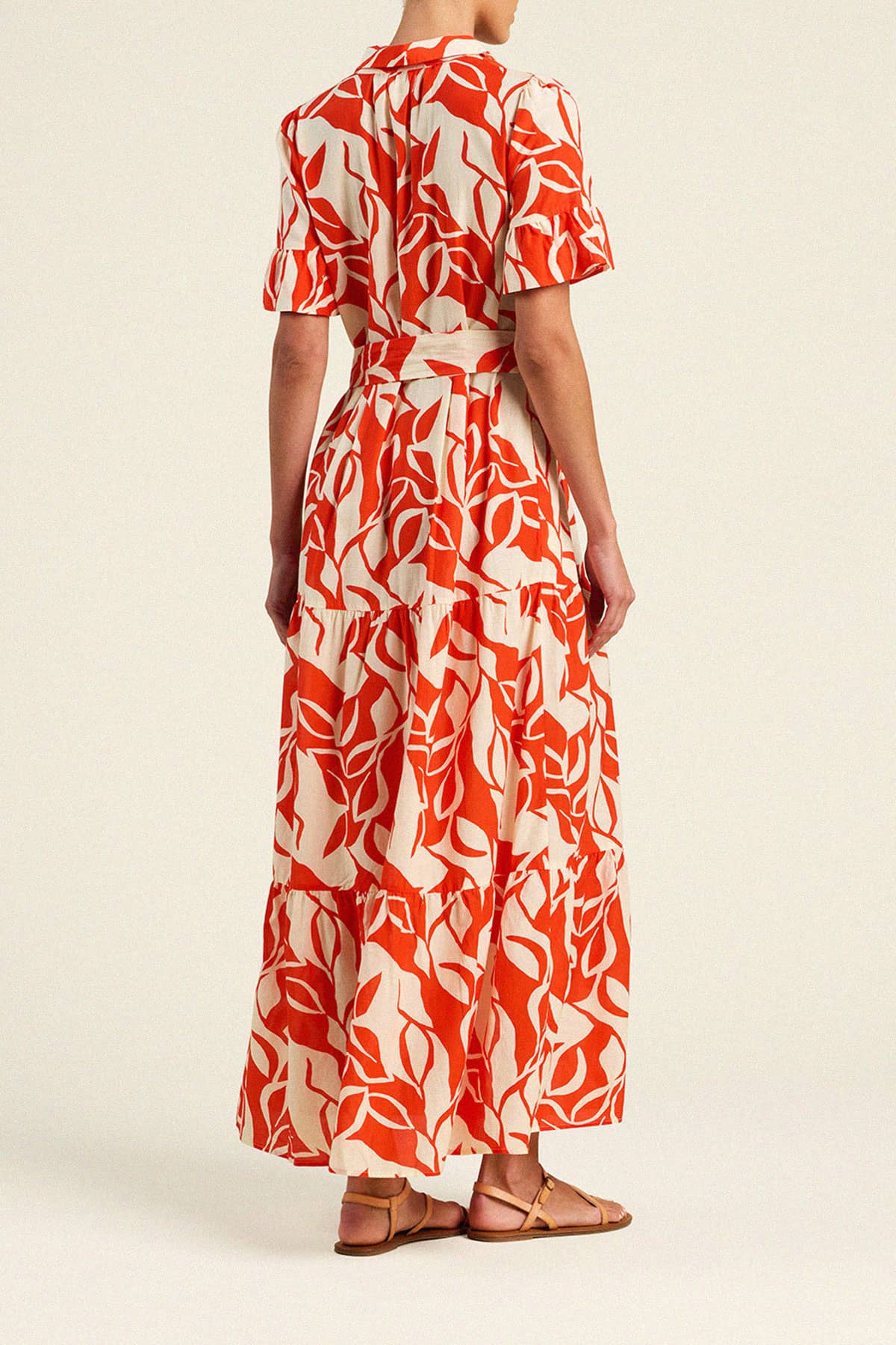 Back view of woman wearing Trovata Martine tiered maxi dress with red and cream leaf print and waist tie.