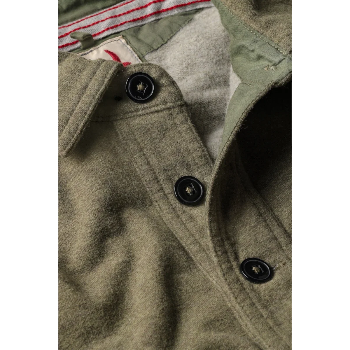 Close-up detail of olive green wool polo shirt with black buttons and striped inner collar