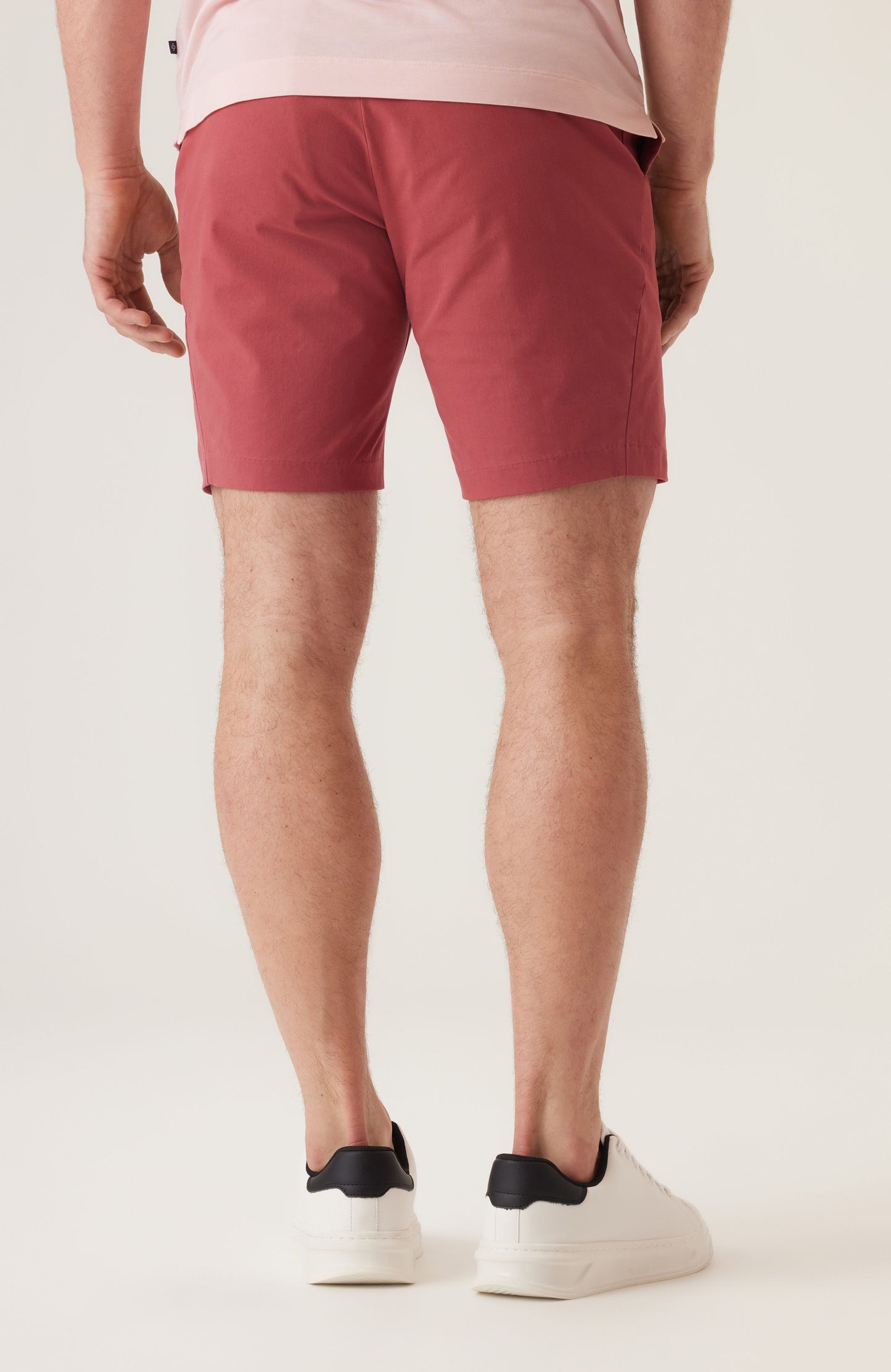 Back view of man wearing red Deke Galaxy Bermuda shorts in stretch twill with white sneakers.