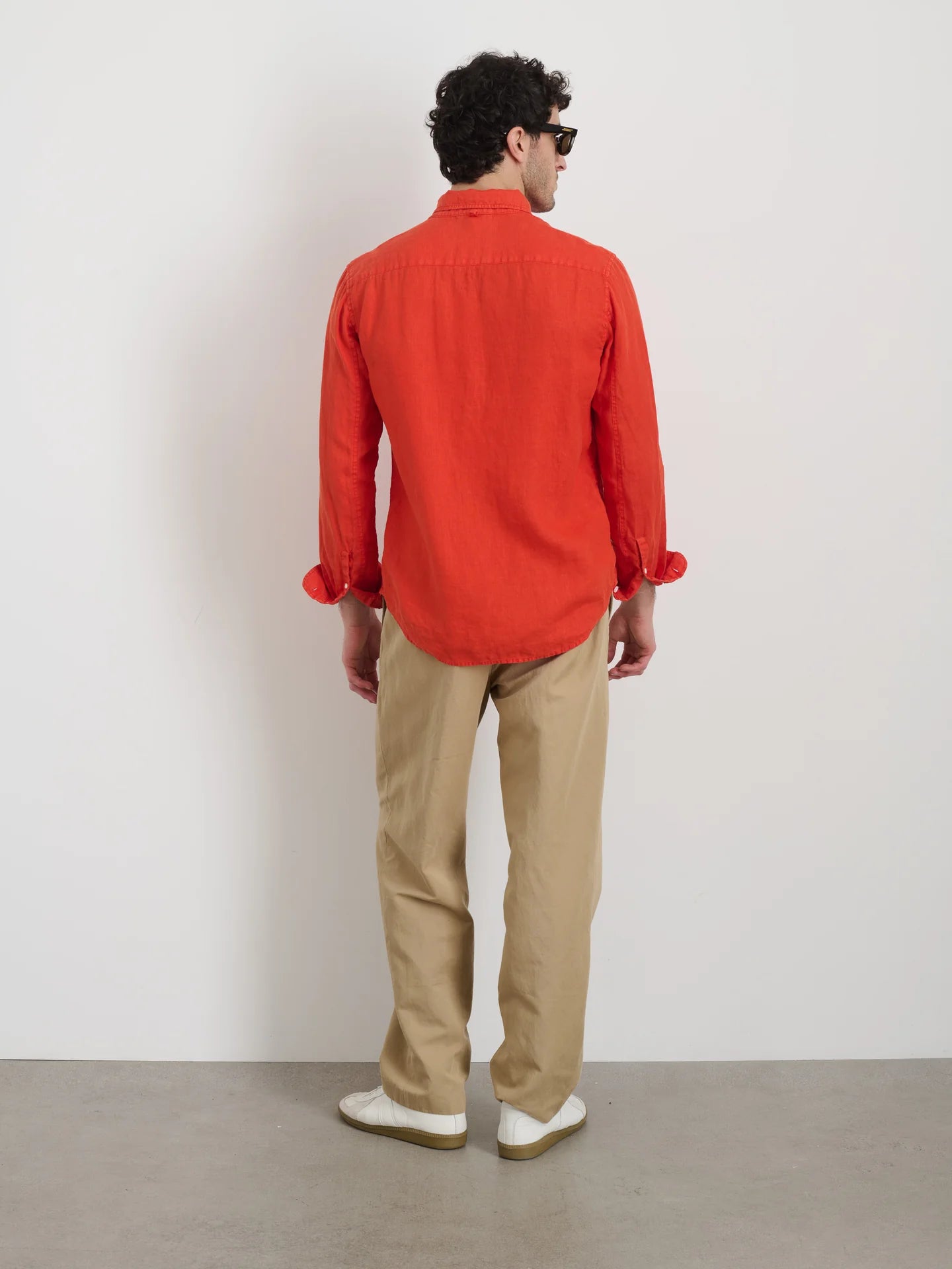 Back view of man wearing Alex Mill tangerine linen button-up shirt with khaki pants and white sneakers.