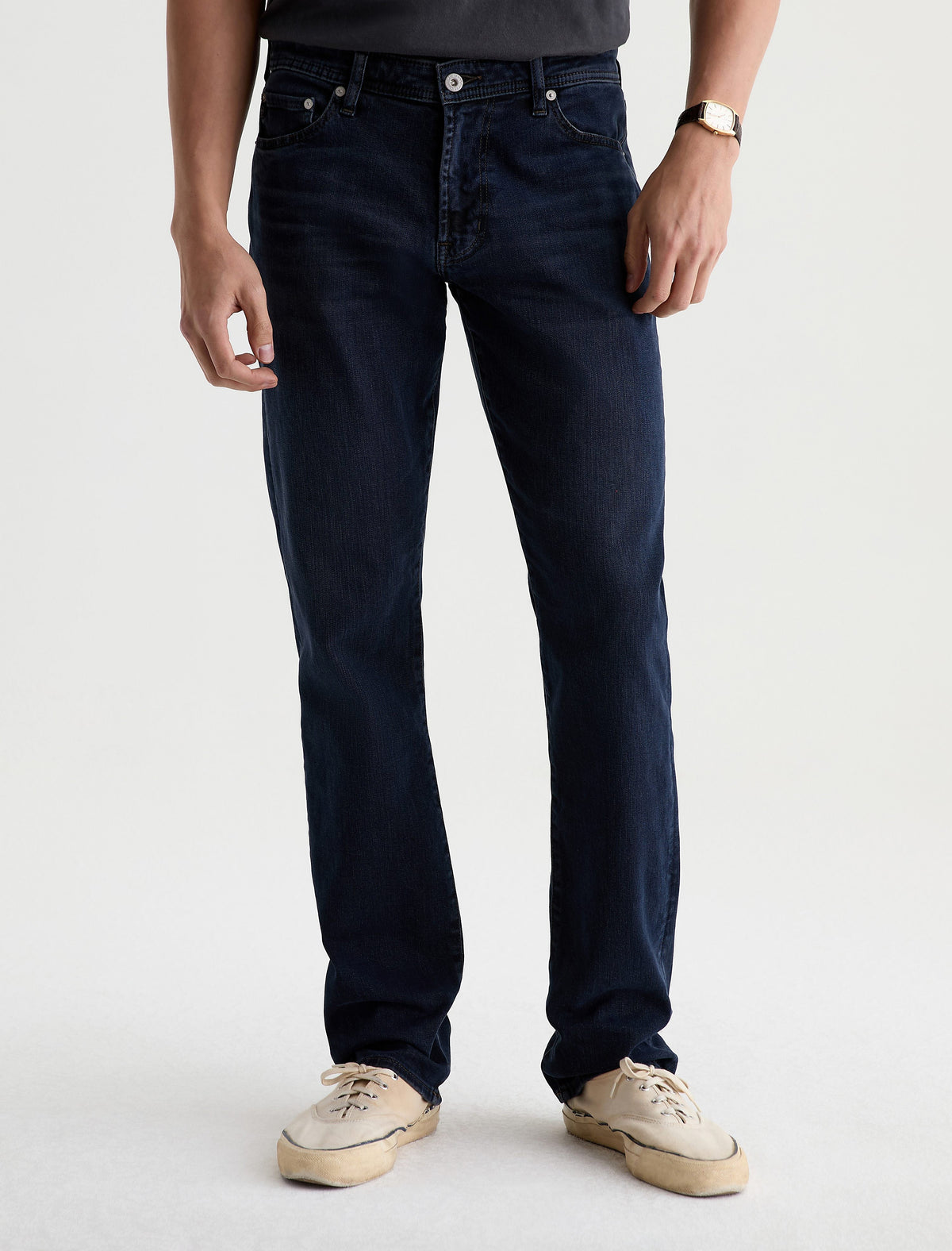 Male model wearing AG Graduate tailored leg jeans in dark indigo wash with sneakers