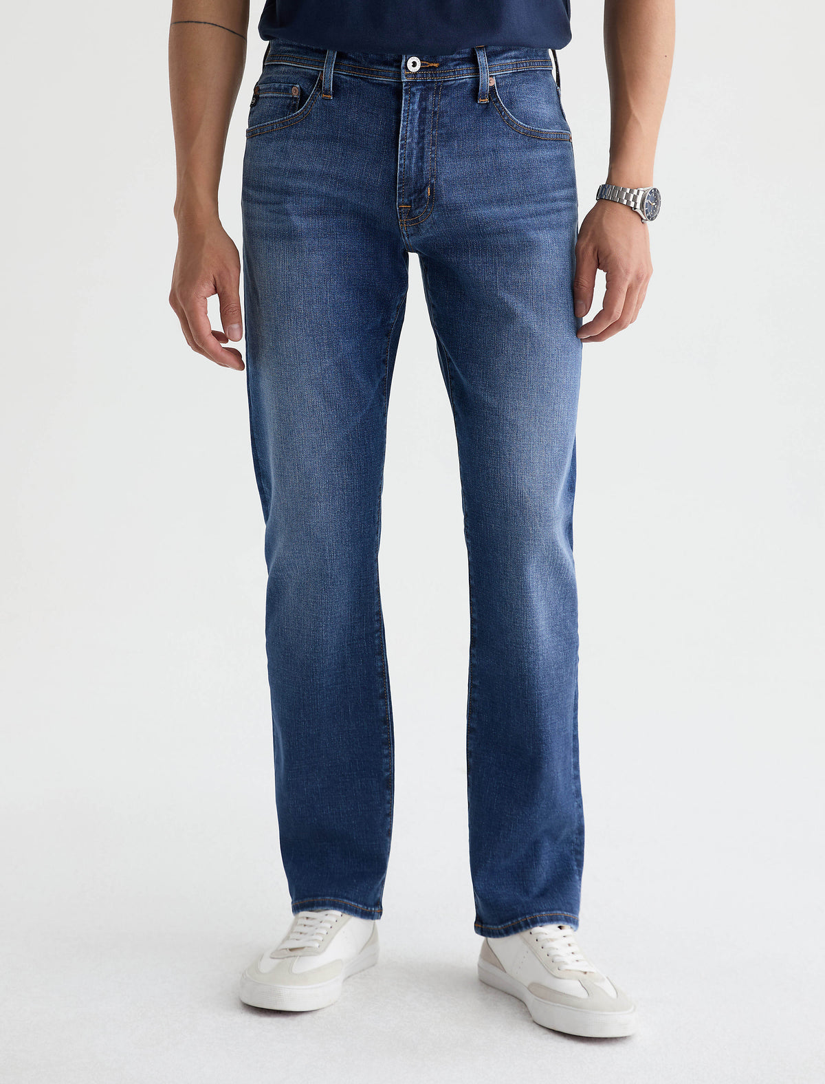Man wearing AG Graduate tailored leg jeans in medium blue wash with white sneakers