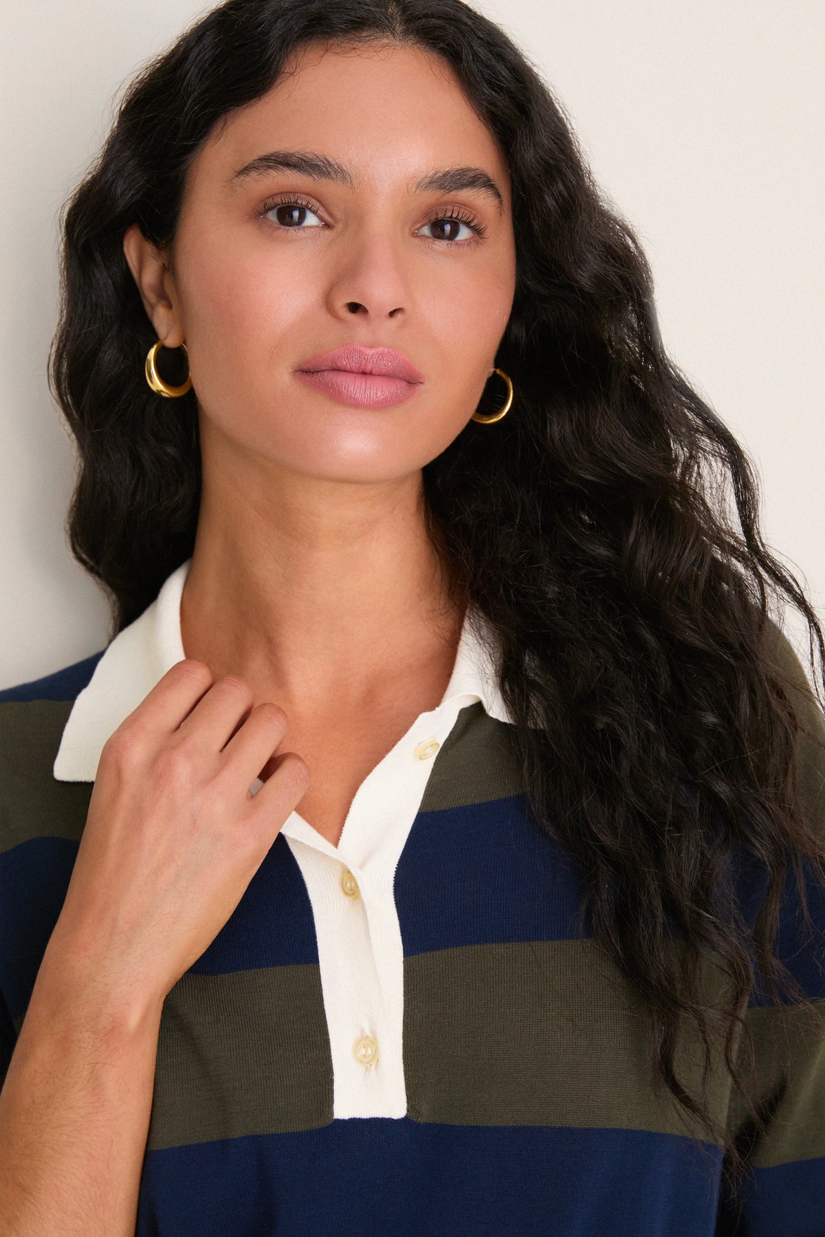 Model wearing navy and olive striped polo sweater with cream collar and gold hoop earrings