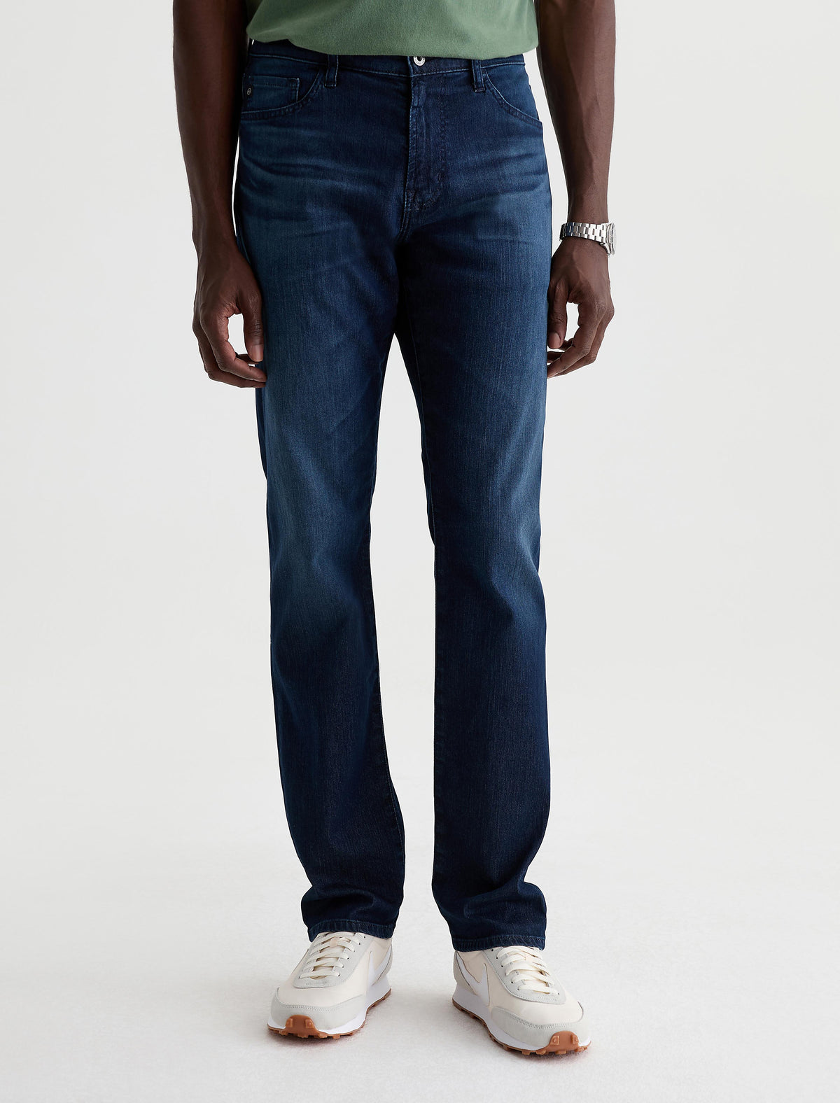 Man wearing dark blue AG Everett slim straight jeans with green shirt and white sneakers