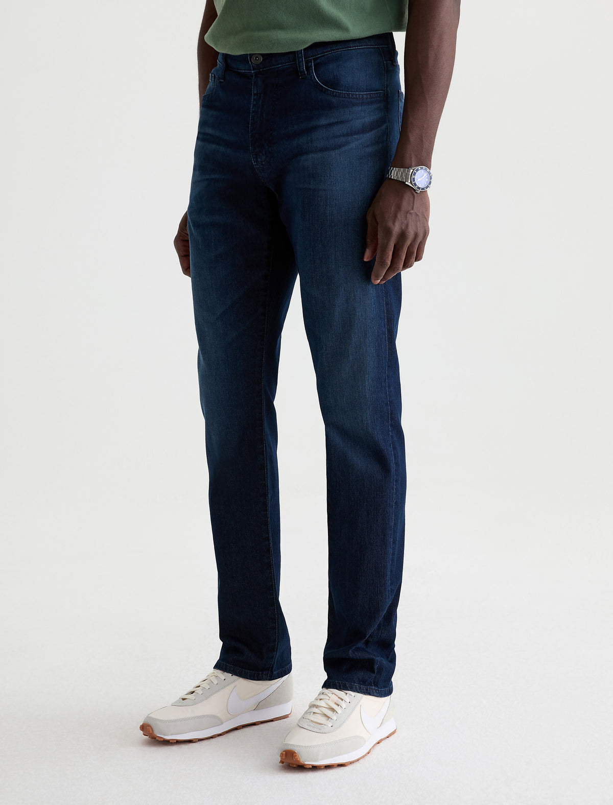Man wearing dark blue AG Everett slim straight jeans with green shirt and white sneakers