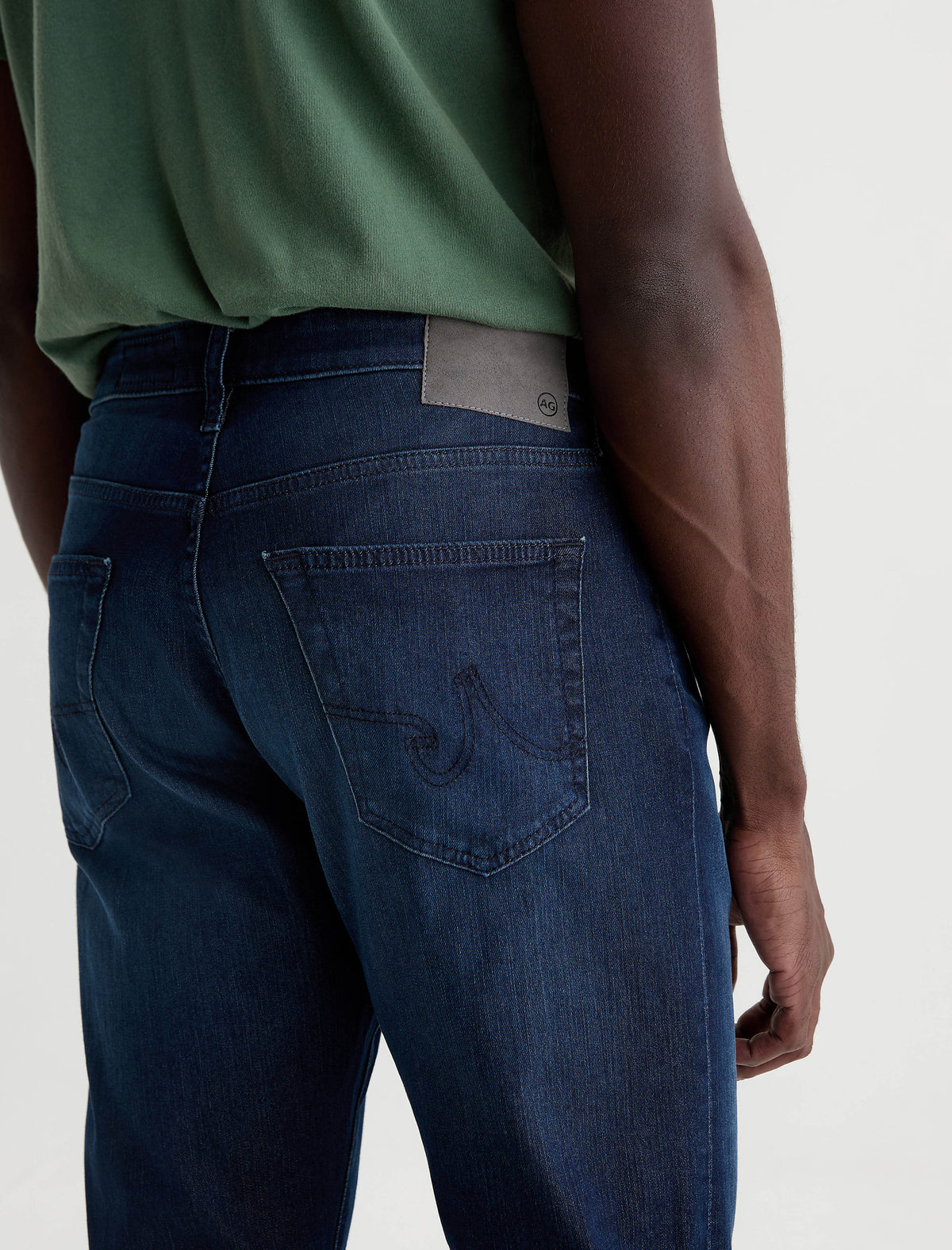 Back view of man wearing AG Everett slim straight jeans in dark blue wash with green t-shirt