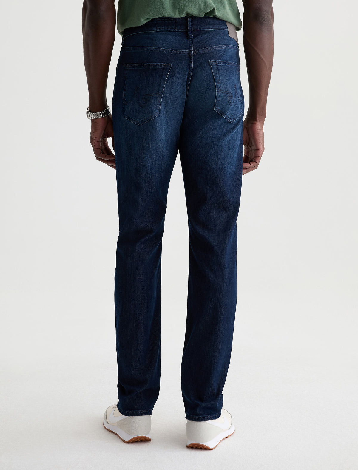 Rear view of model wearing dark blue AG Everett slim straight jeans with green shirt and white sneakers