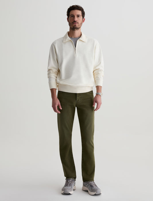 Male model wearing AG Everett slim straight jeans in olive green with white quarter-zip sweatshirt