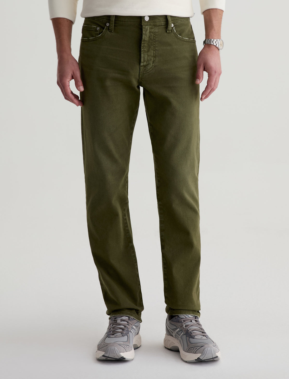 Man wearing AG Everett slim straight jeans in olive green with grey sneakers