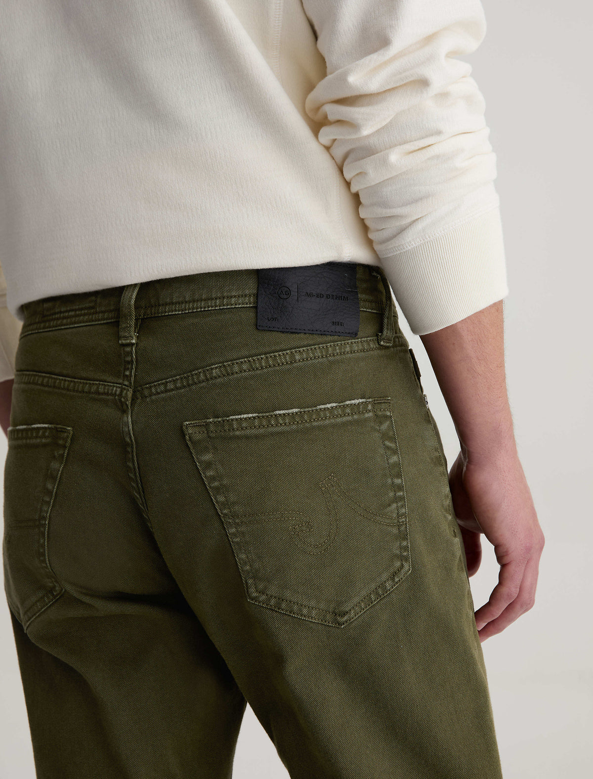 Close-up back view of AG Everett slim straight jeans in olive green with leather patch label