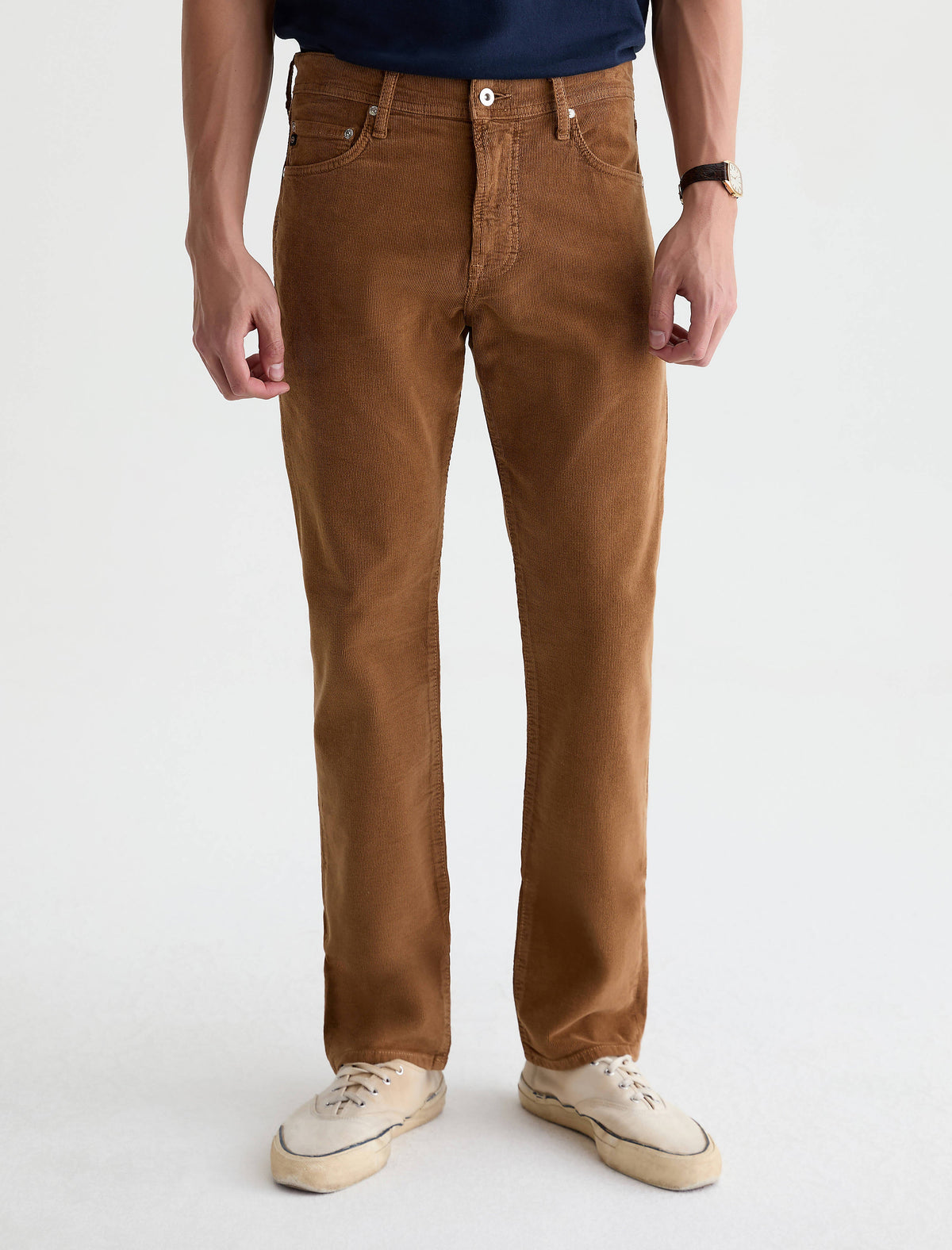 Man wearing AG Everett slim straight corduroy pants in bronze tan color with white sneakers