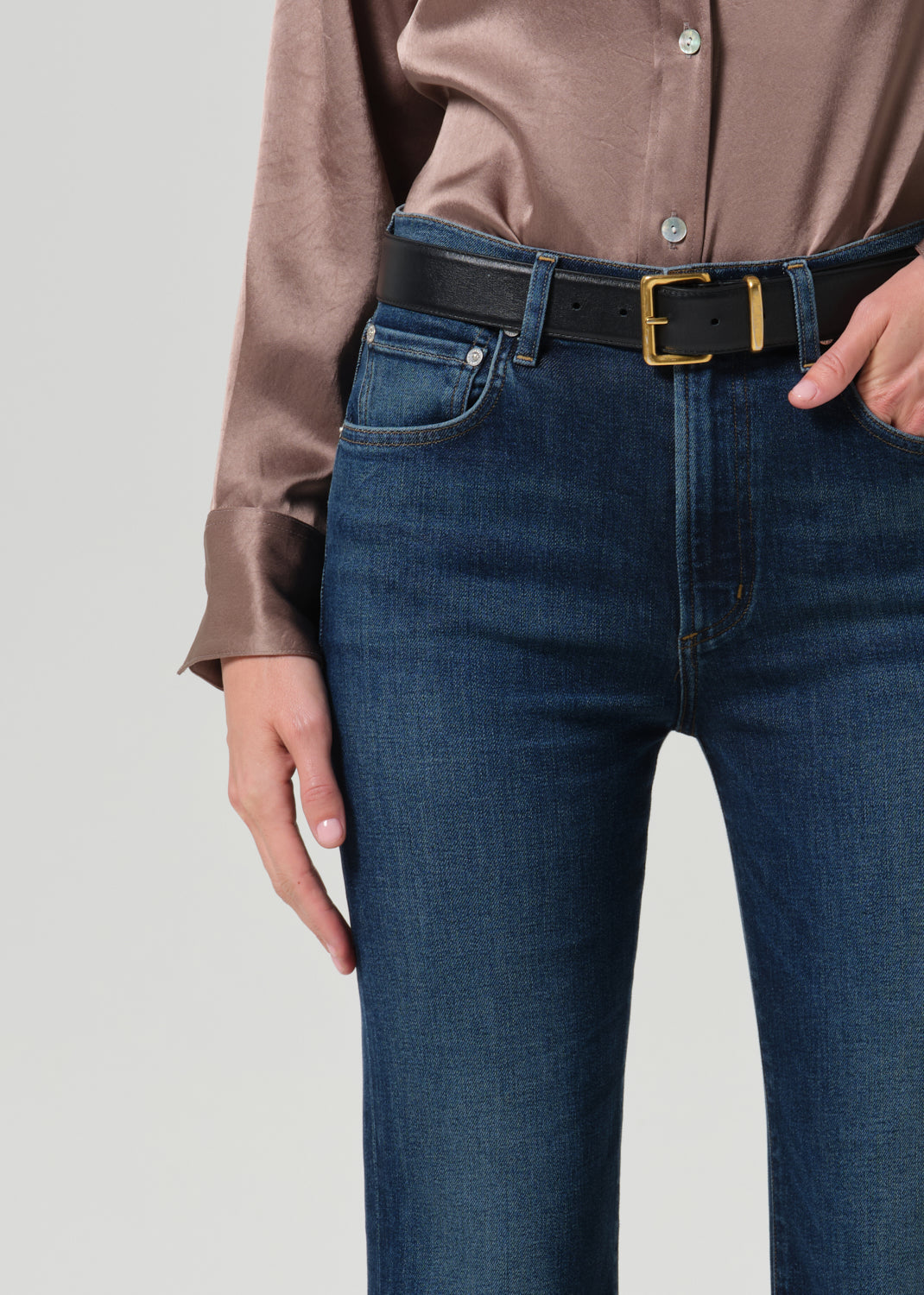 Close-up of high rise bootcut dark indigo jeans with black leather gold-buckle belt