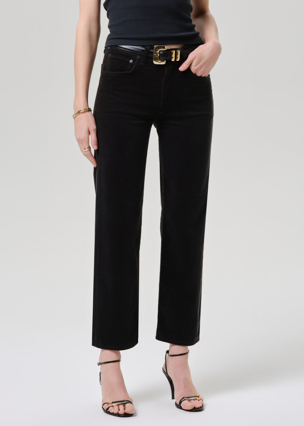 Model wearing Citizens of Humanity Palma straight-leg black corduroy jeans with gold belt and strappy heels
