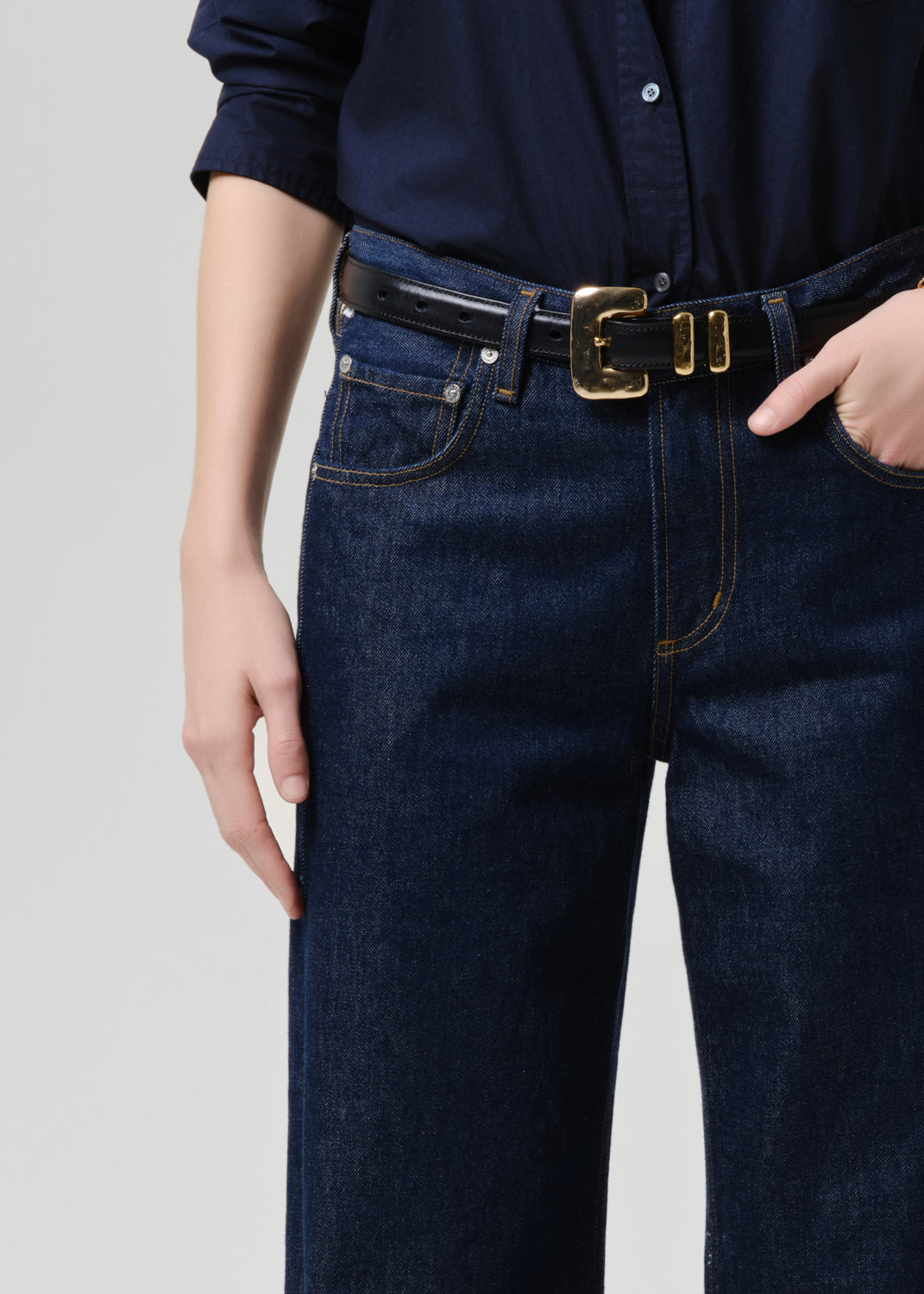 Close-up of dark indigo straight-leg jeans with black leather gold-buckle belt