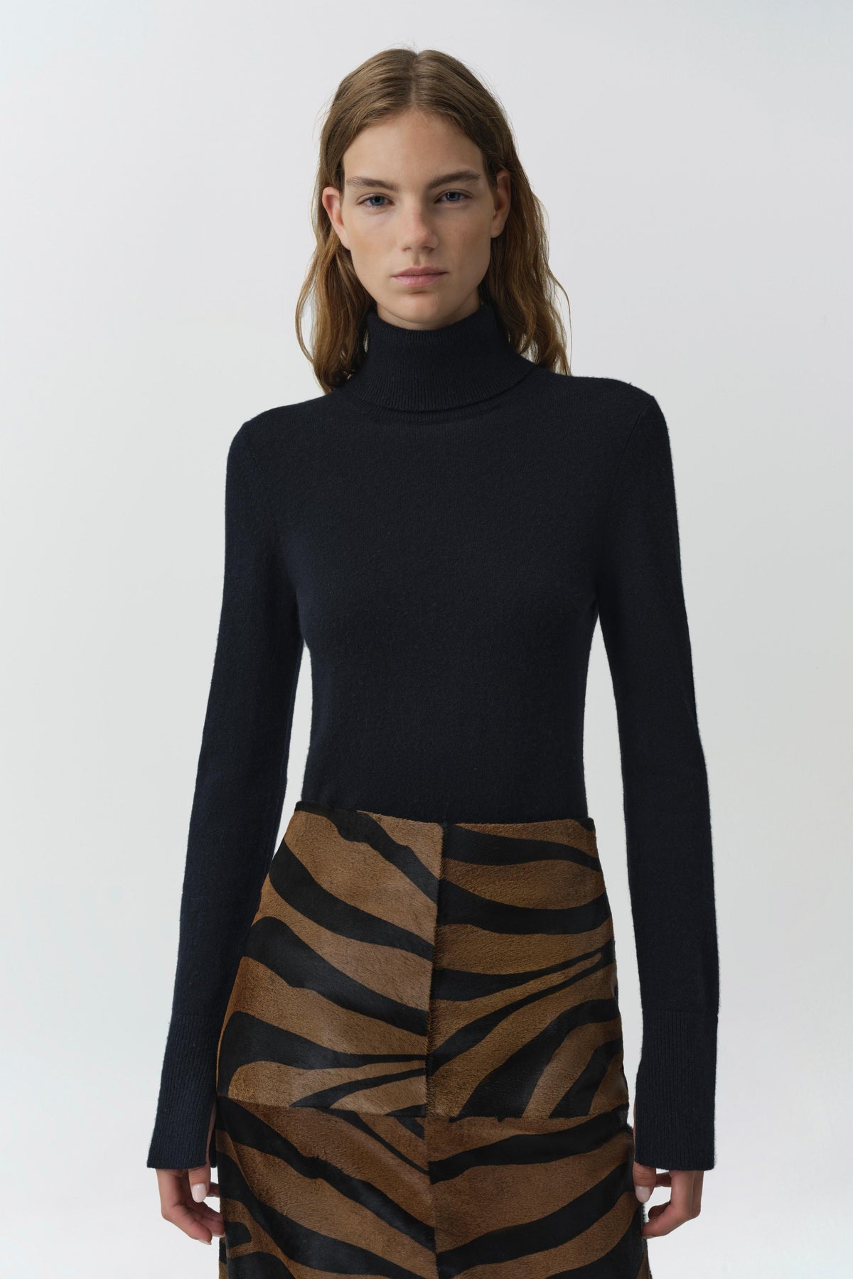Model wearing fitted black cashmere turtleneck sweater with long sleeves paired with animal print skirt