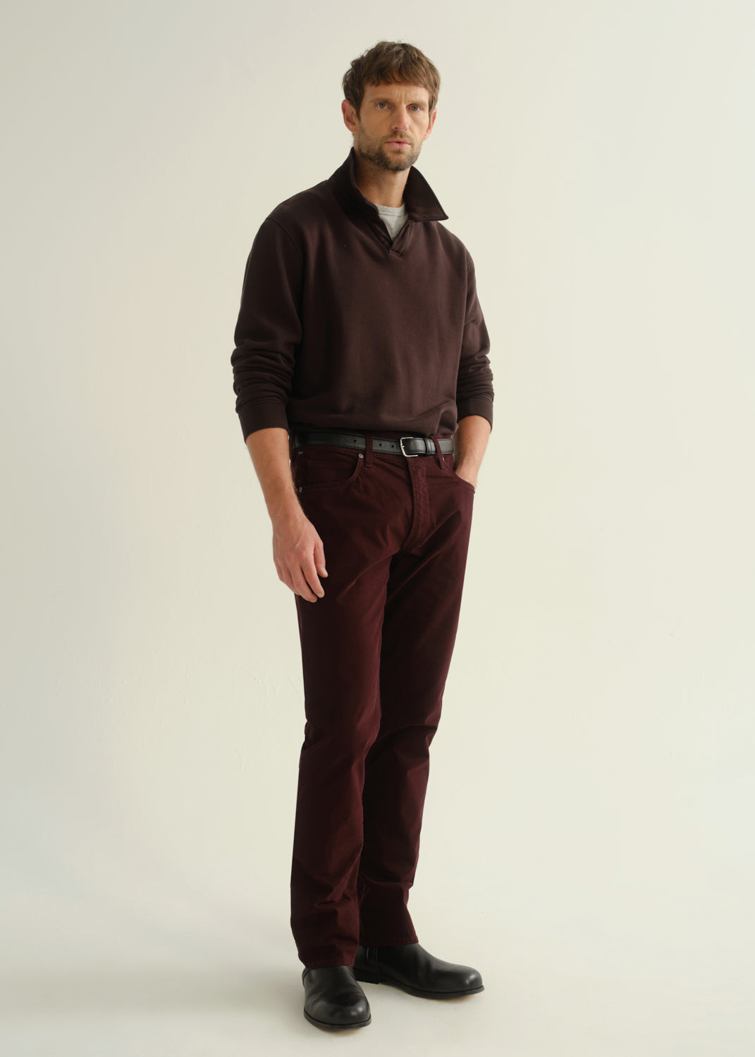 Male model wearing Citizens of Humanity Gage slim straight burgundy sateen pants with dark pullover
