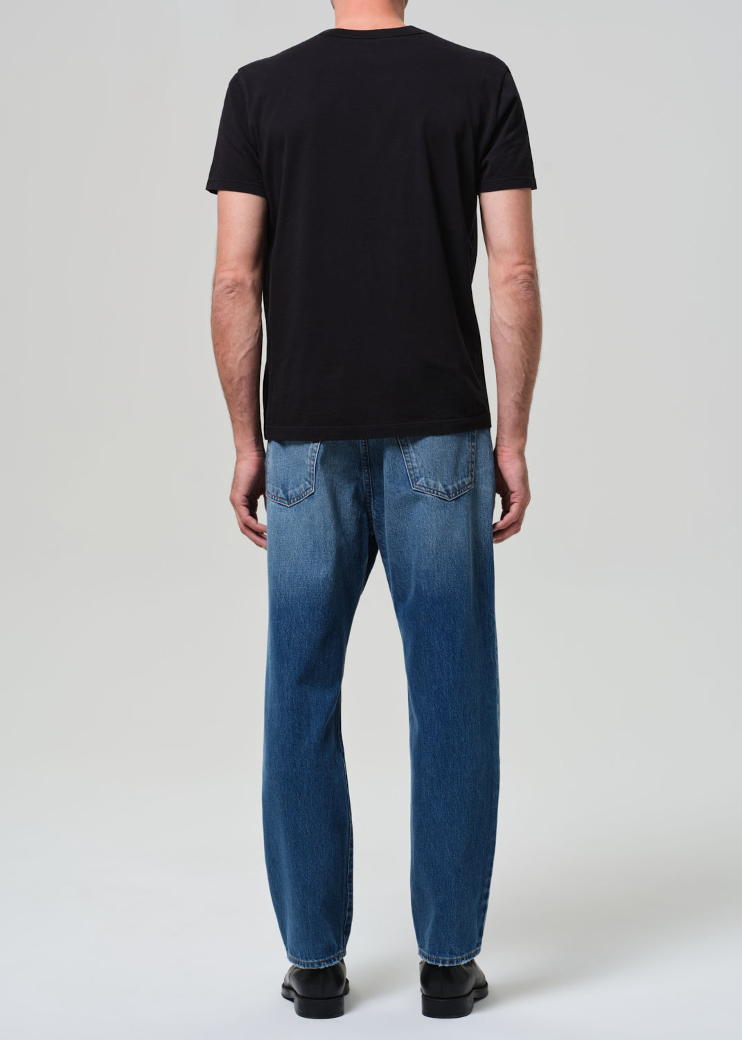 Man wearing mid blue straight leg jeans with black t-shirt from behind