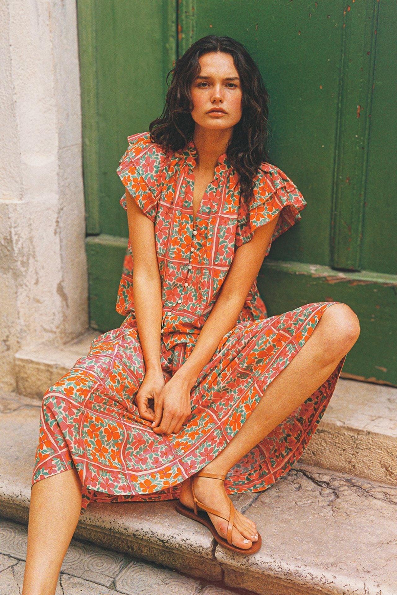 Woman wearing orange and green floral patterned blouse and matching pants sitting on stone steps