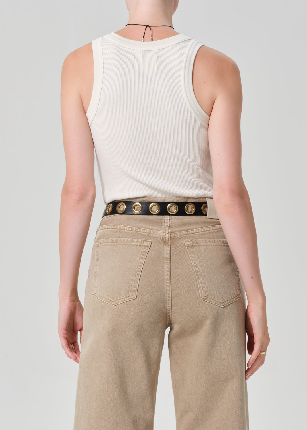 Back view of model wearing beige ribbed tank top and tan pants with studded belt