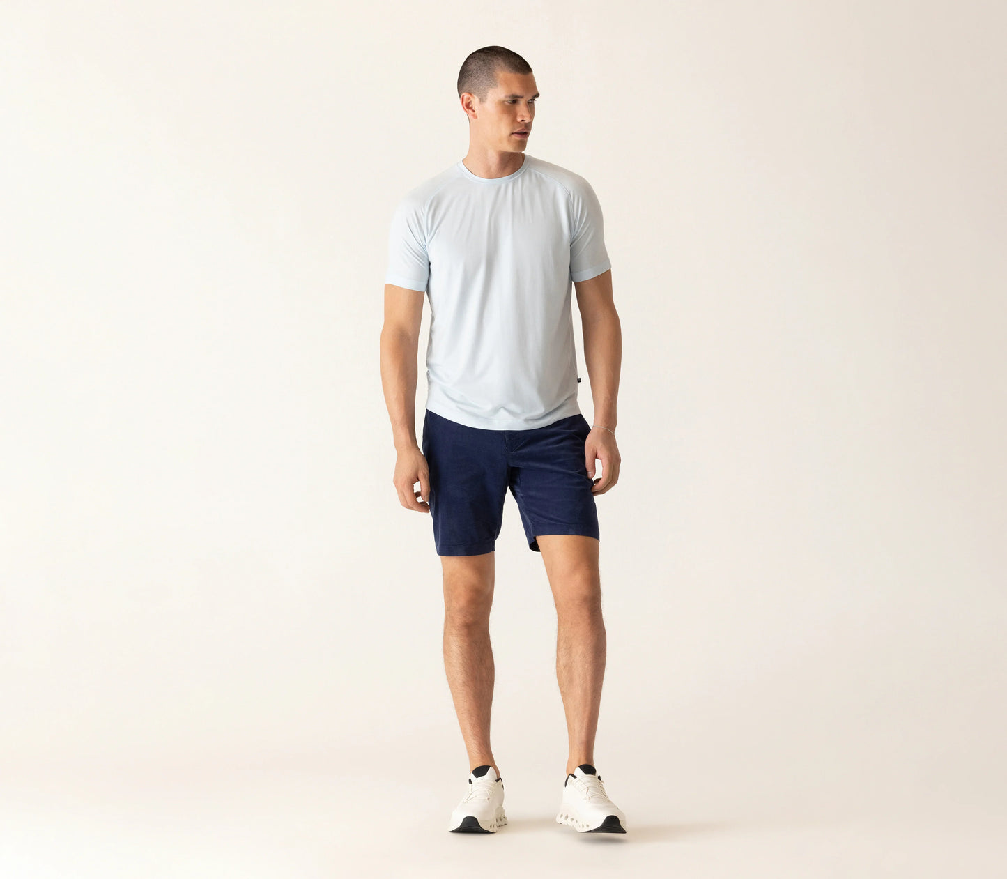 Man wearing light blue t-shirt and dark navy corduroy bermuda shorts against beige background