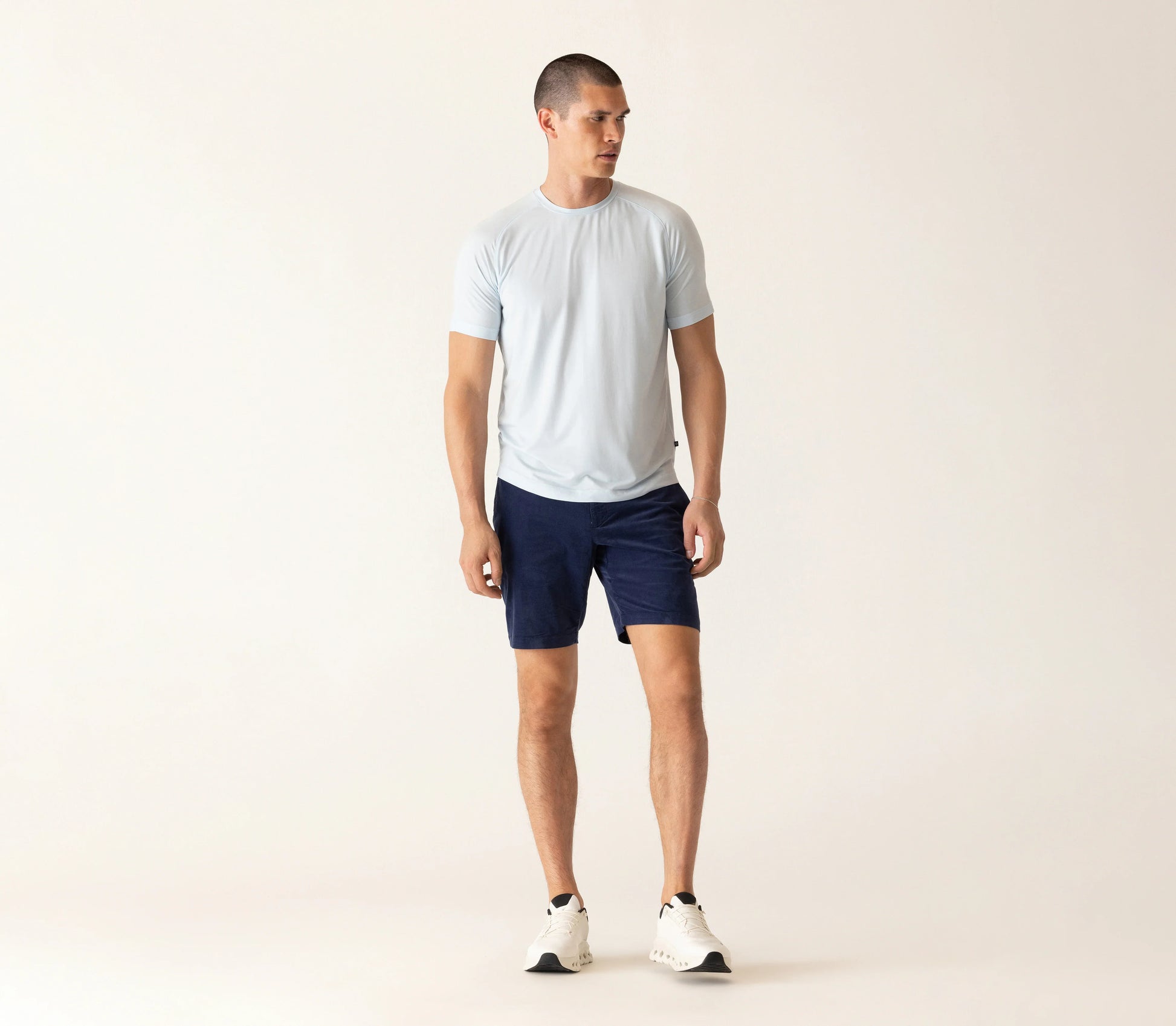 Man wearing light blue t-shirt and dark navy corduroy bermuda shorts against beige background