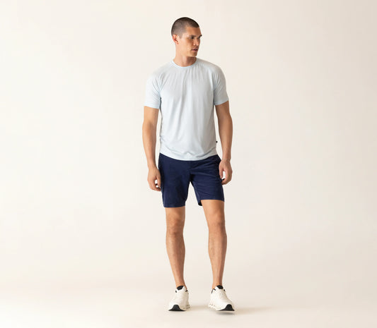 Man wearing light blue t-shirt and dark navy corduroy bermuda shorts against beige background