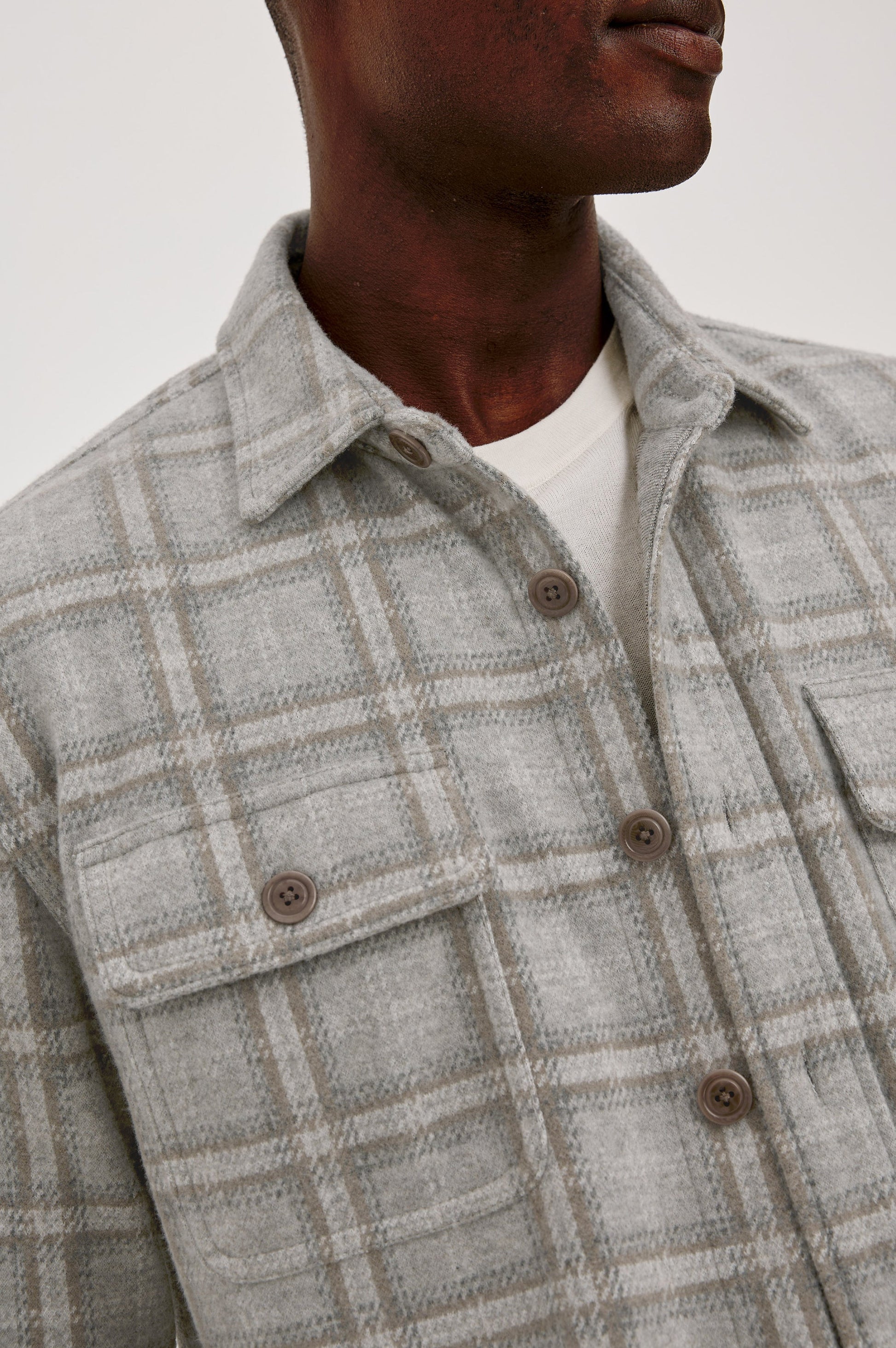 Close-up of male model wearing grey plaid flannel overshirt with brown buttons and chest pocket