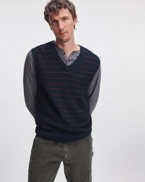 Male model wearing navy striped knit vest over grey henley with olive trousers