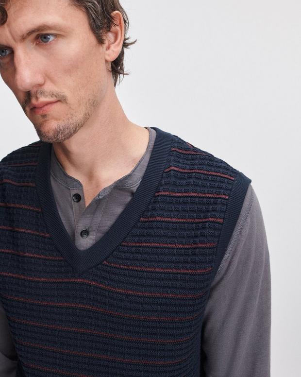Man wearing navy striped knit vest over grey henley long sleeve shirt