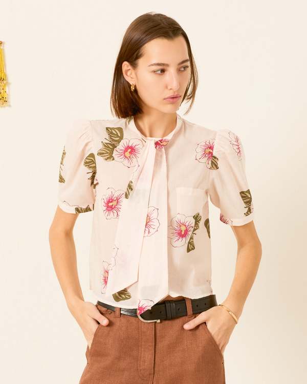 Woman wearing off-white floral blouse with pink hibiscus print and brown pants