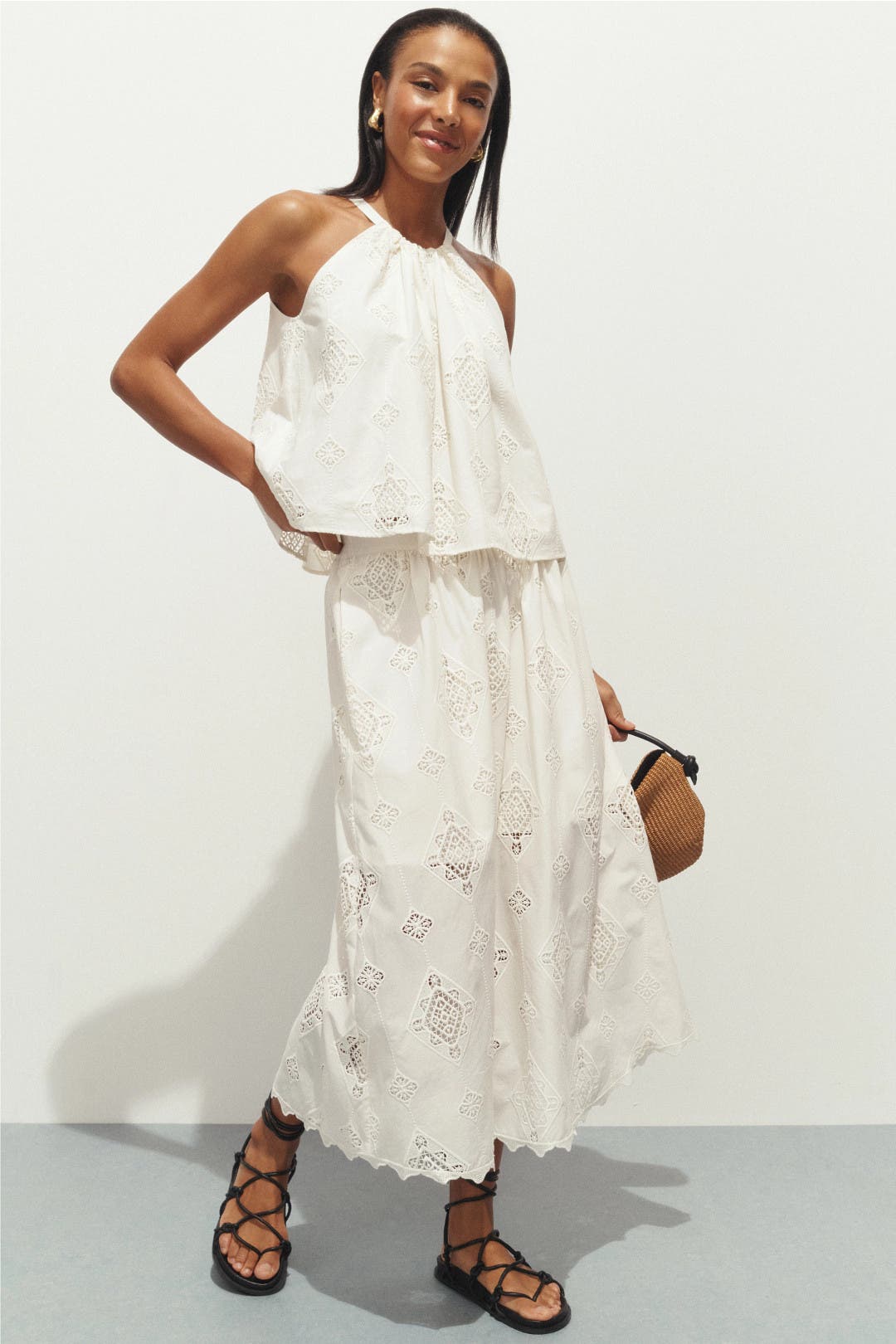 Model wearing white embroidered midi skirt with matching halter top and woven clutch