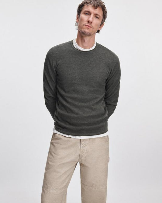 Male model wearing dark army green merino wool crewneck sweater with beige pants