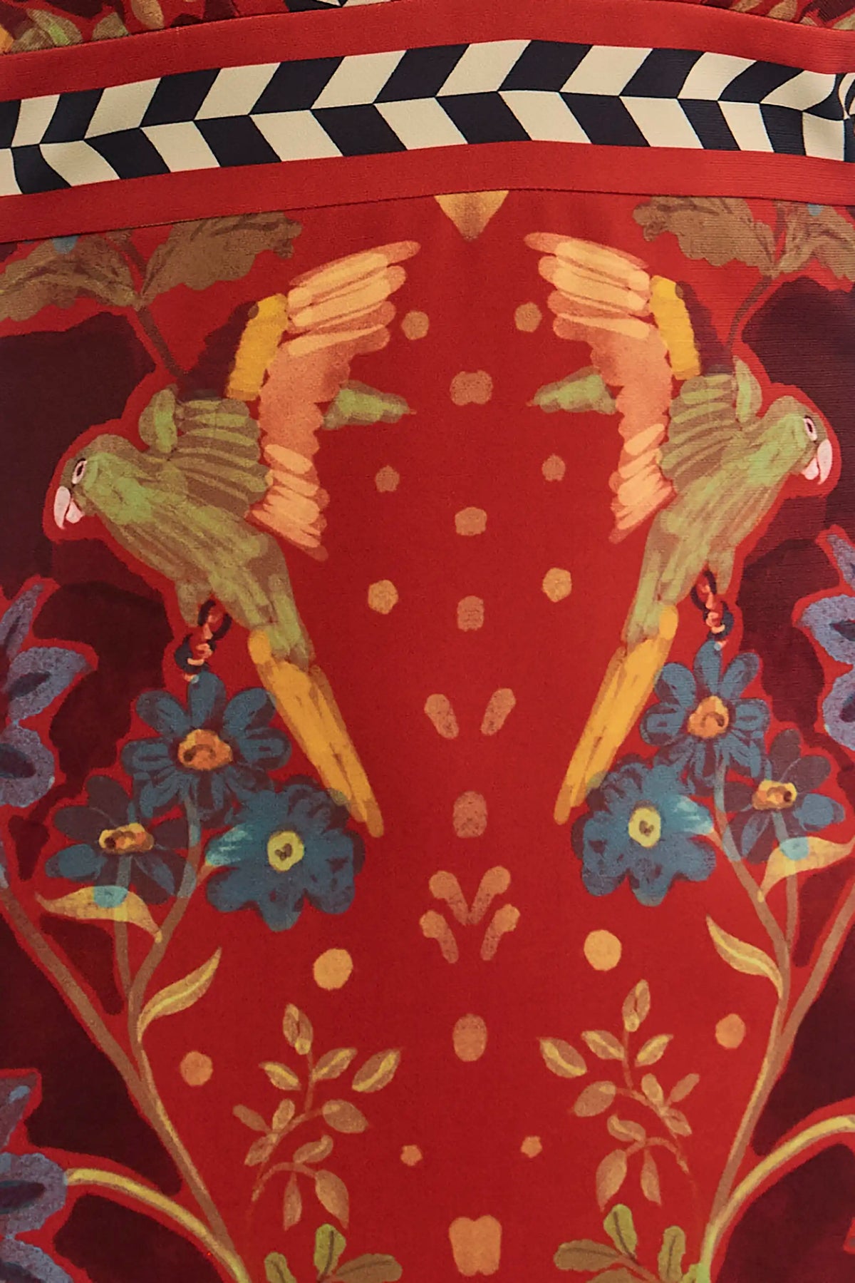 Close-up of maroon skirt fabric featuring mirrored green parrots, blue flowers, and chevron border trim