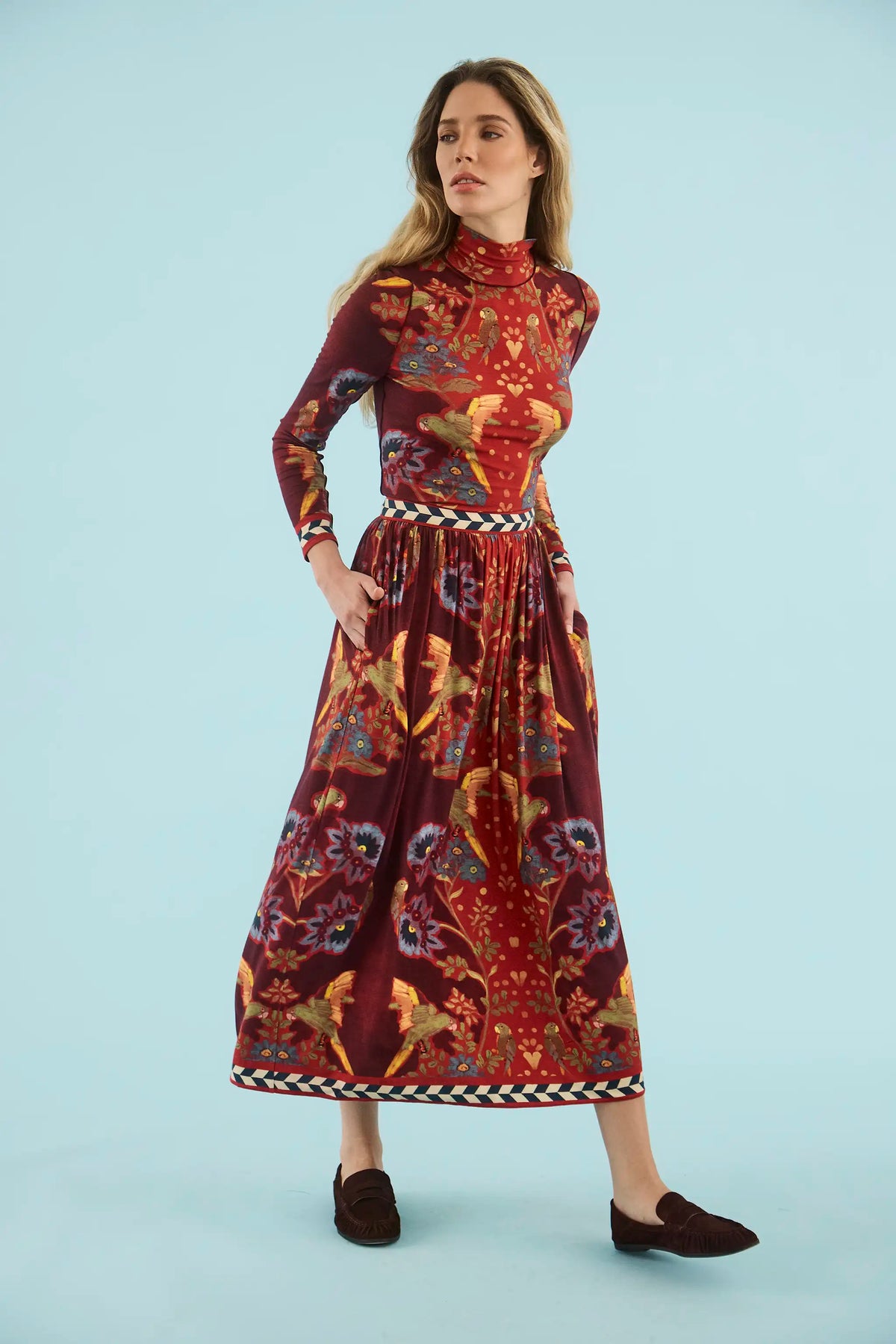 Model wearing maroon bird and floral print midi skirt with matching turtleneck top and dark loafers