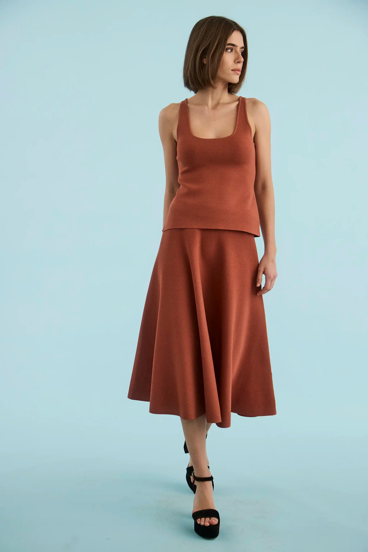 Model wearing Hunter Bell Joan midi skirt in rust terracotta with matching tank top and black heels