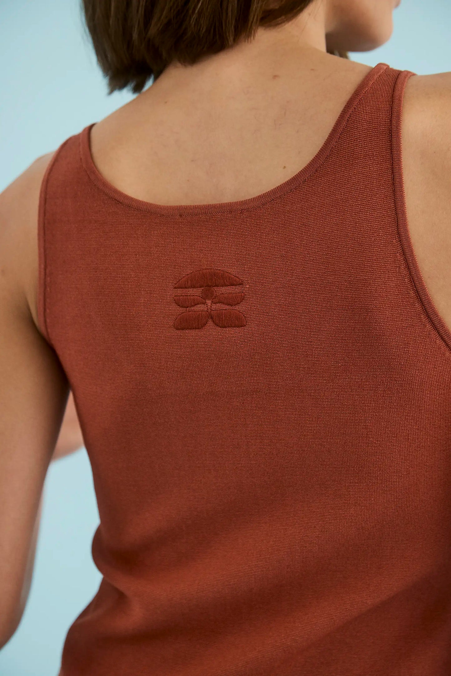 Back view of rust-colored sleeveless cami tank top with embroidered floral logo detail