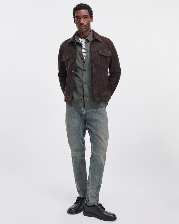 Male model wearing dark green denim workwear shirt layered under brown suede jacket with grey jeans