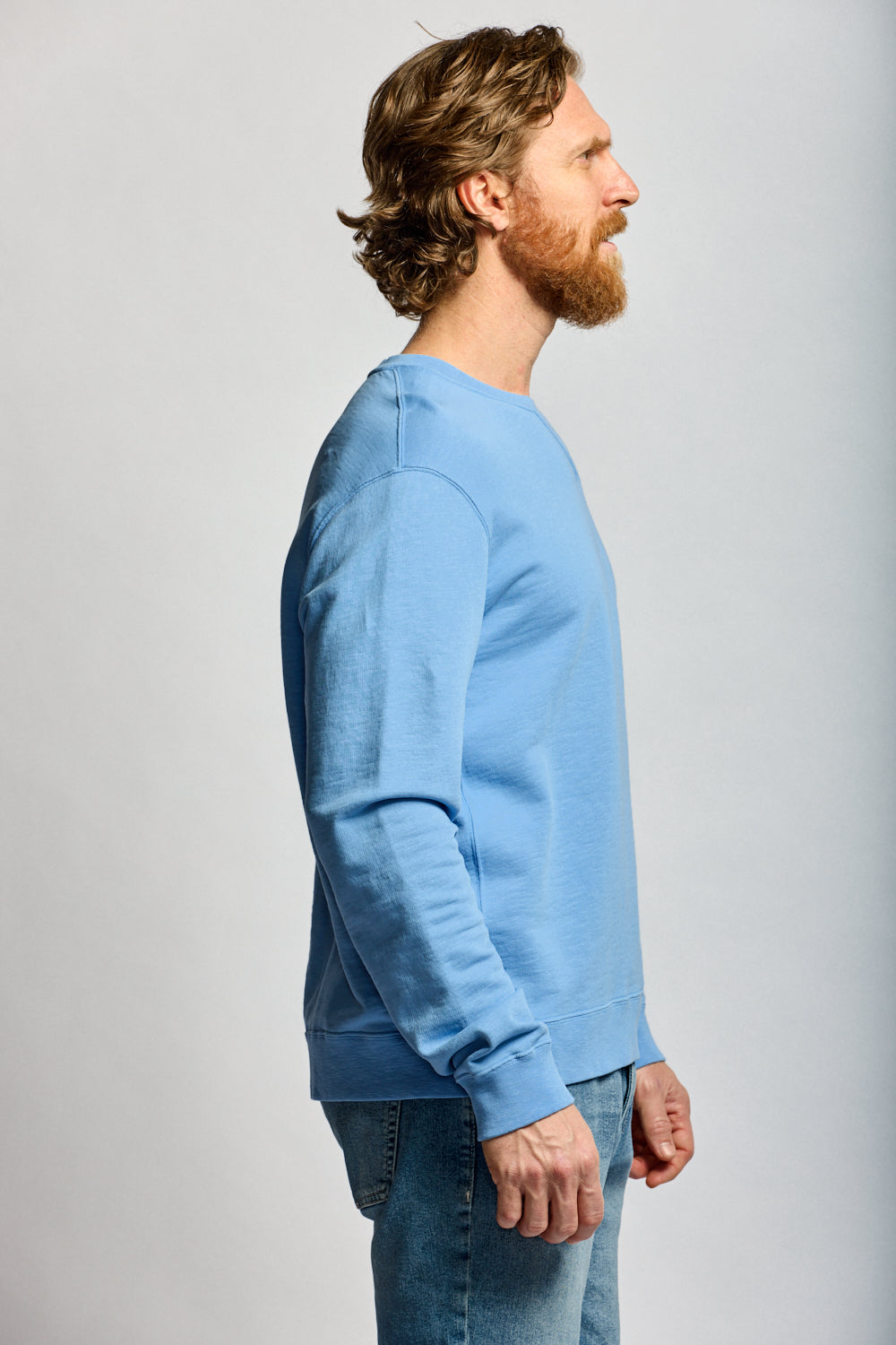Man wearing Easy Mondays azure blue slub cotton crewneck sweatshirt with jeans, side profile view