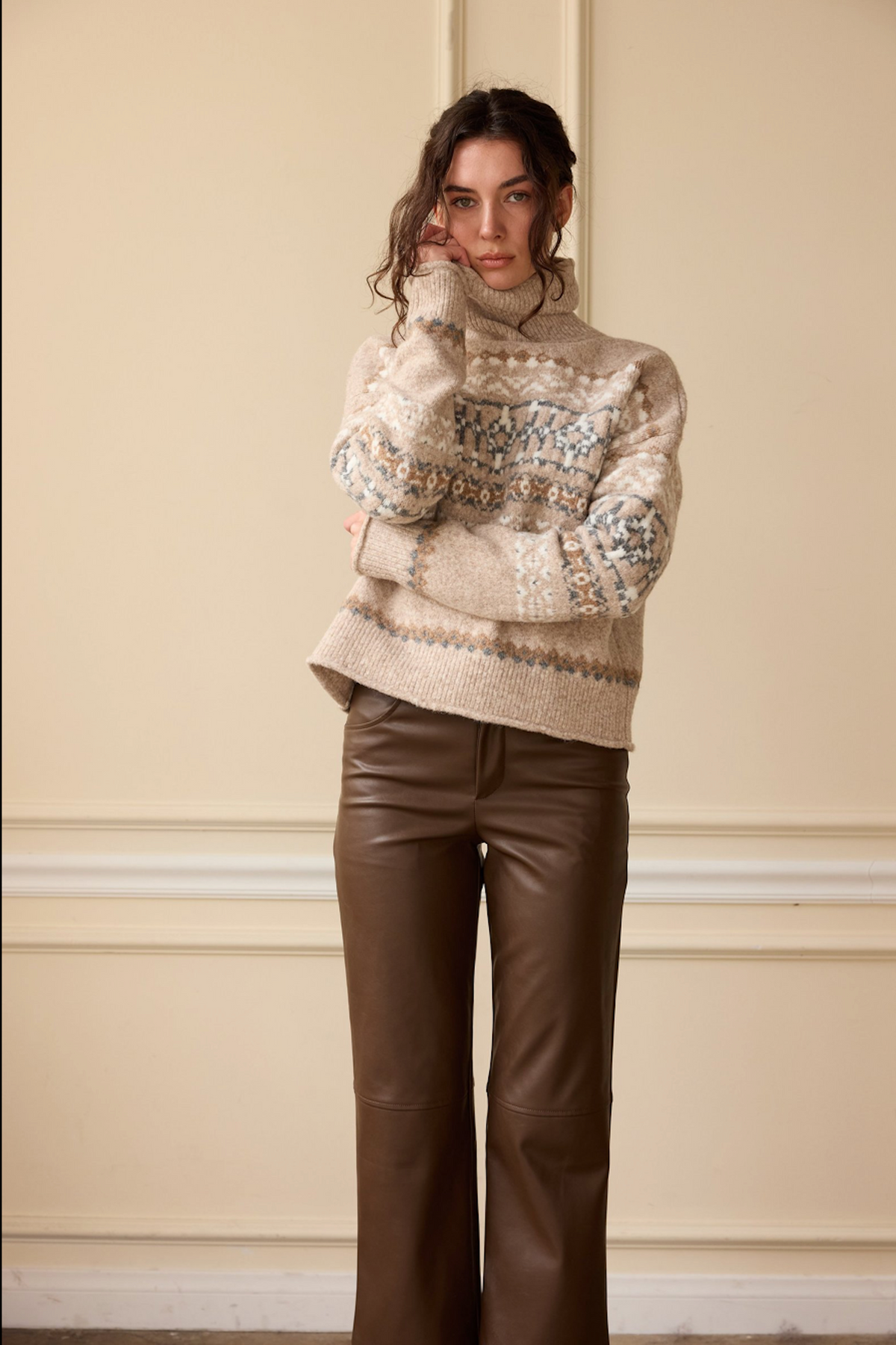 Model wearing a beige Fair Isle turtleneck sweater with brown leather flare pants