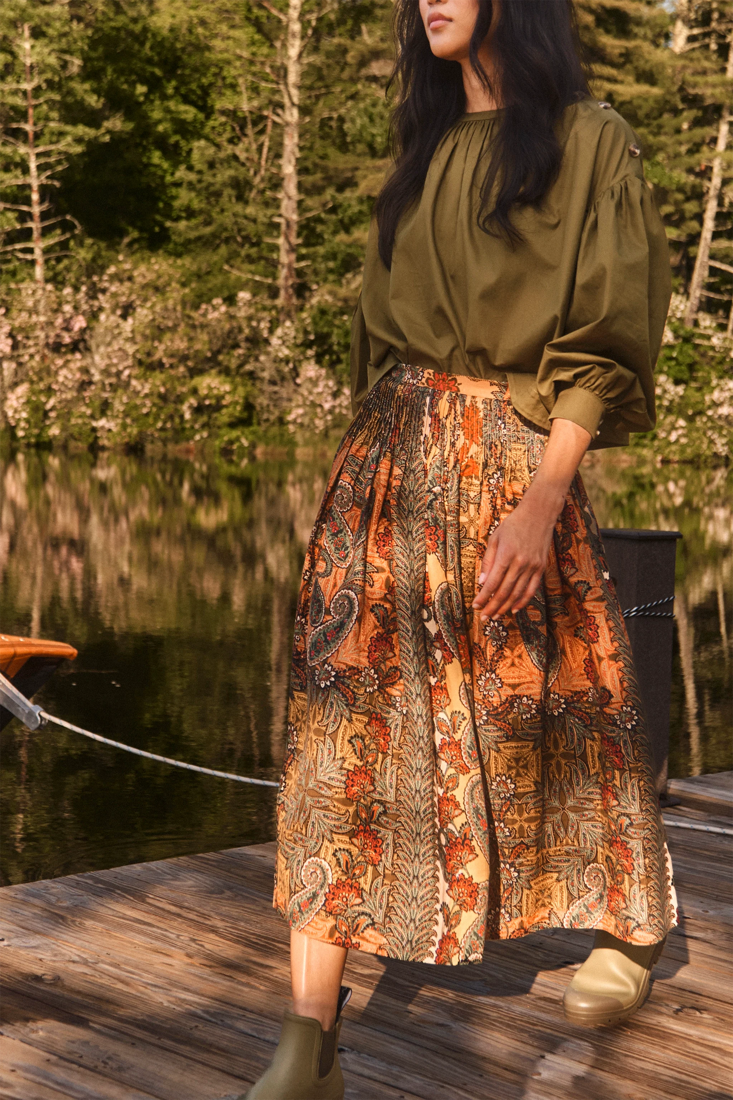 Model wearing Hunter Bell Fallon midi skirt in golden orange Highland Tapestry paisley print on dock
