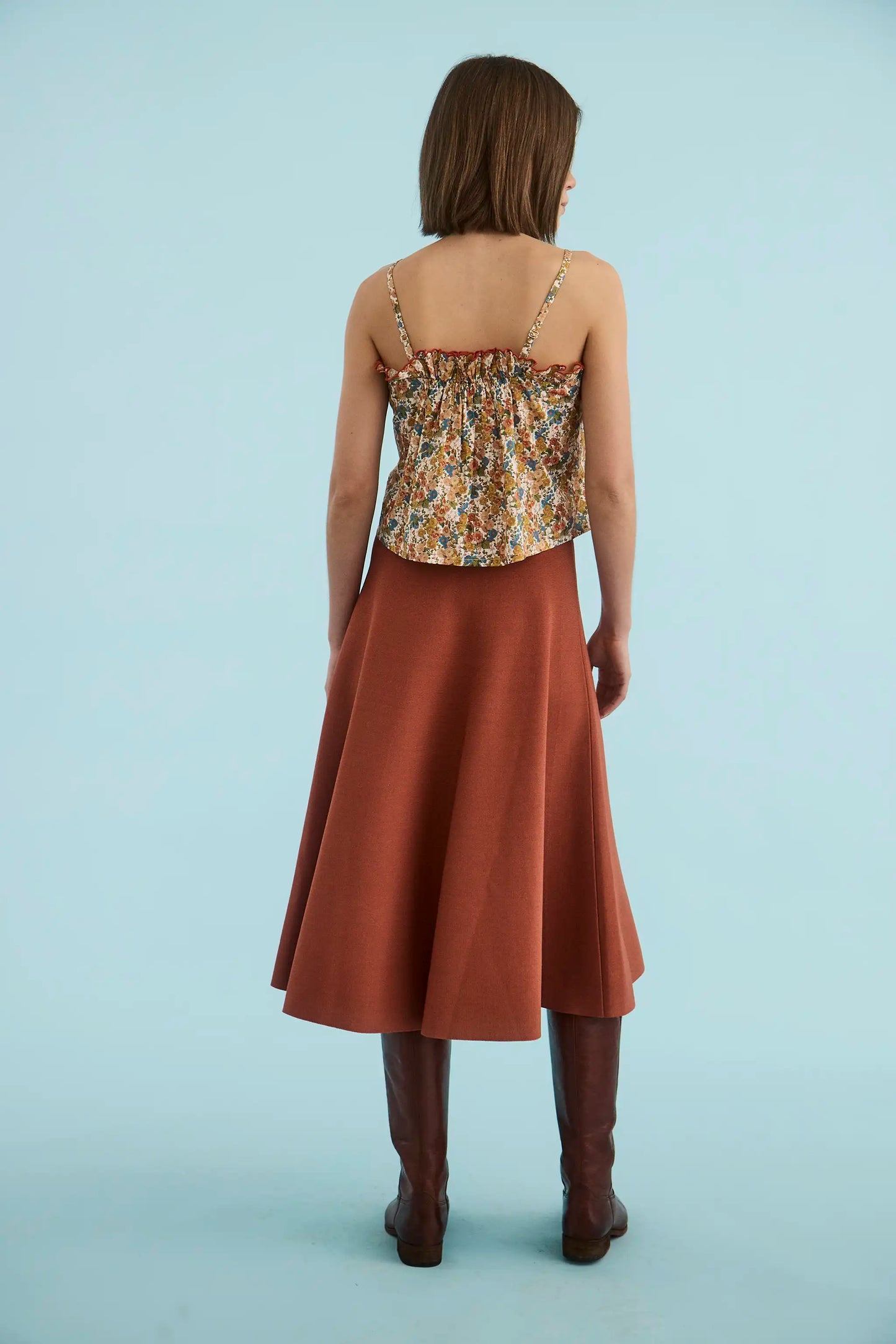 Model wearing Hunter Bell Joan Skirt in rust terracotta midi length with floral cami top and brown boots, back view