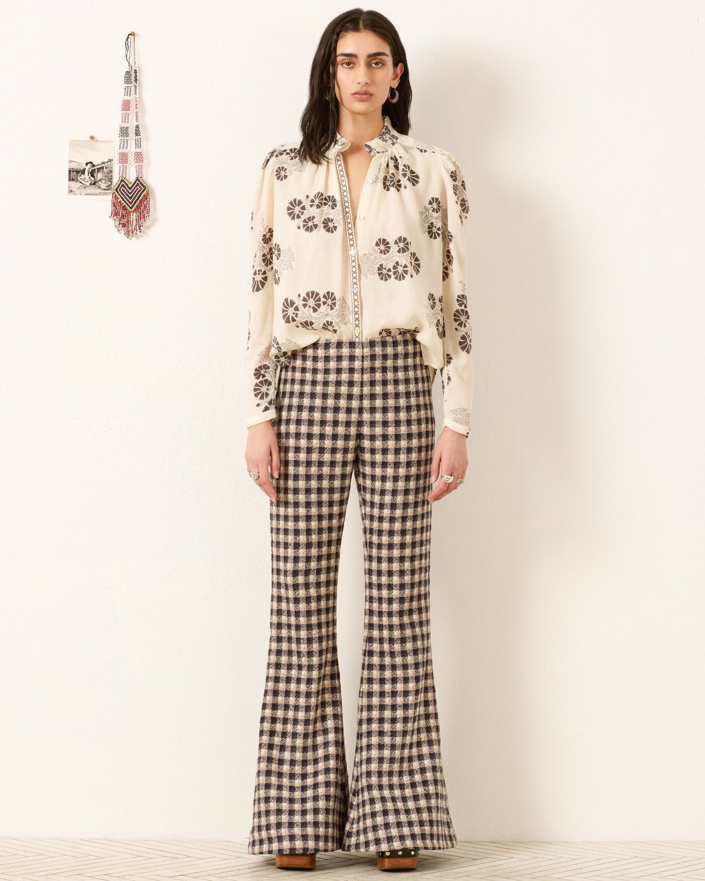Model wearing white floral print blouse with decorative trim and checkered flare pants